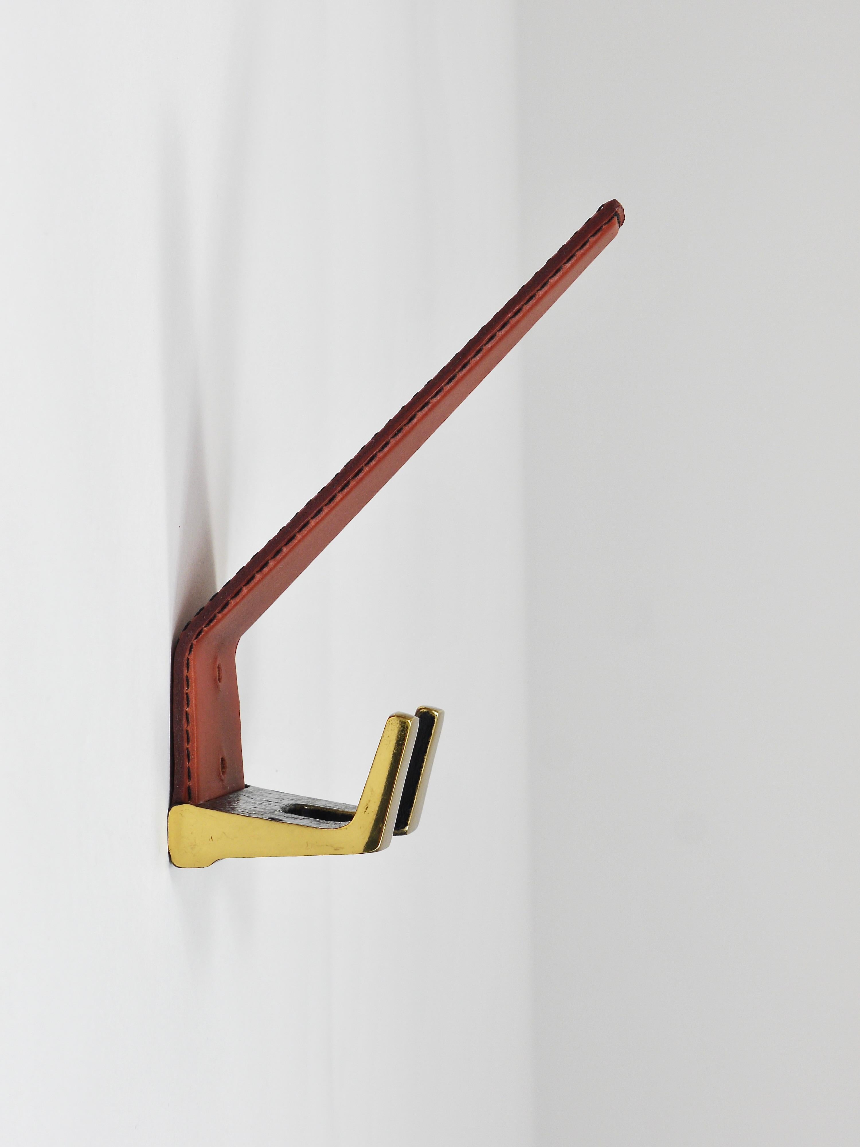 A set of four beautiful vintage Modernist wall coat hooks. Crafted in Vienna, Austria during the 1950s, these hooks are made of solid brass, partly black patinated and partly polished, and adorned with medium brown tan leather. These pieces are