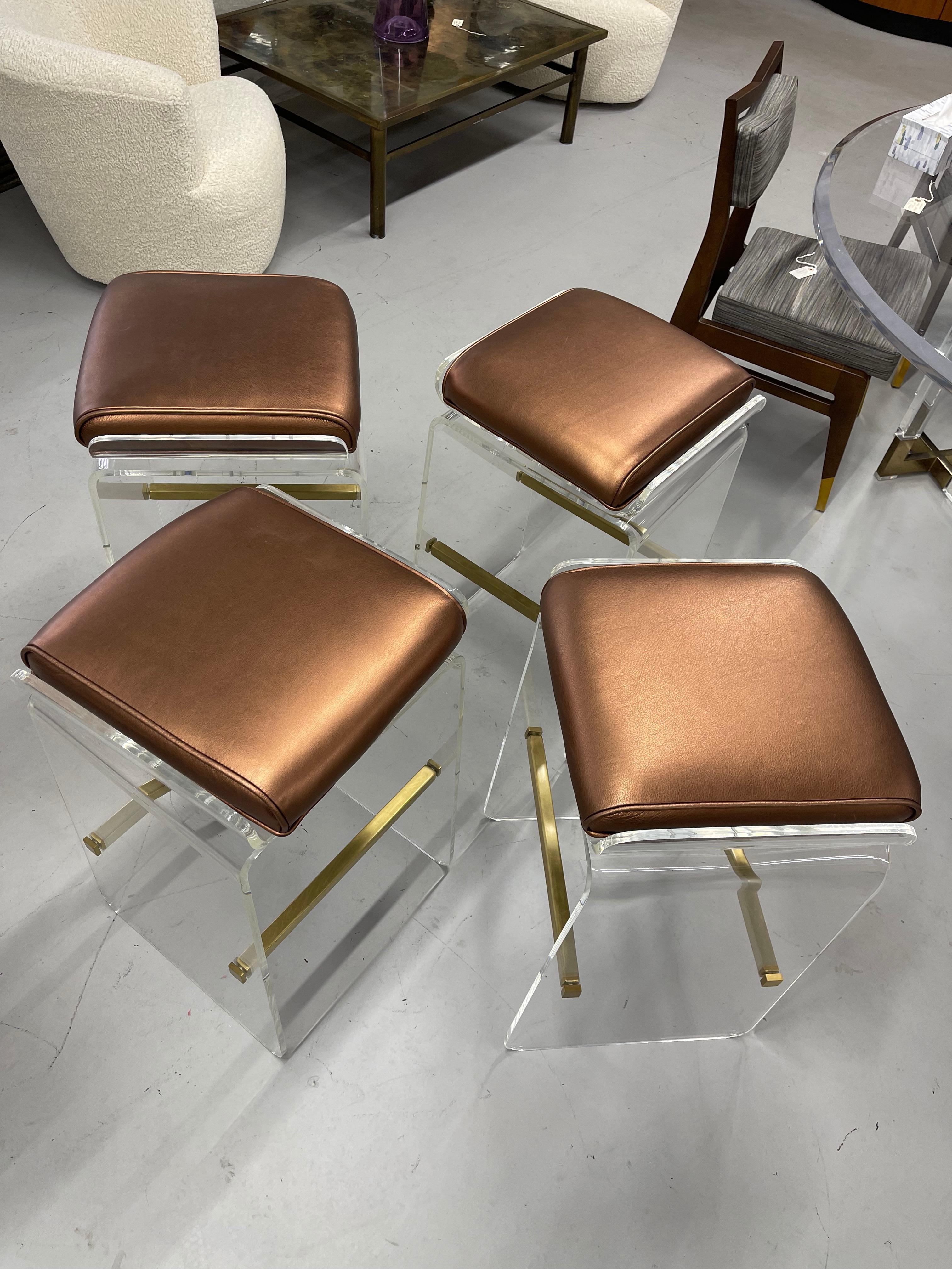 A pretty set of 4 Charles Hollis Jones Lucite and brass bar stools with copper colored leather seats. The seats swivel. These are vintage stools that have been re-upholstered and reconditioned. They are in good condition with only some minor marks