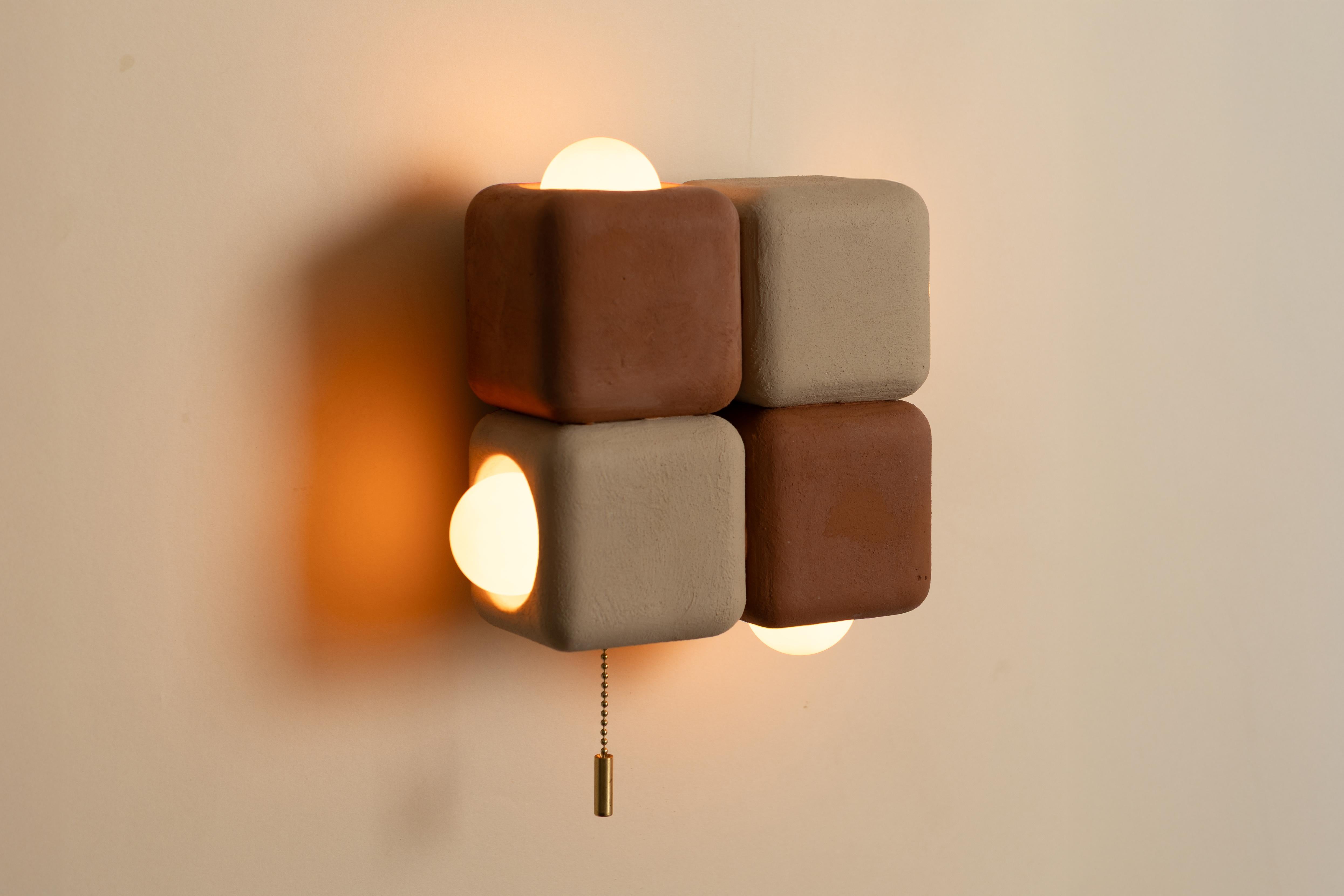 L'applique a 4 cubi trasforma la semplicità geometrica in un'applique scultorea. Quattro cubi ammorbiditi formano una griglia stretta, i cui bordi arrotondati conferiscono calore a una composizione minimale. Tra le forme, le lampadine a globo si