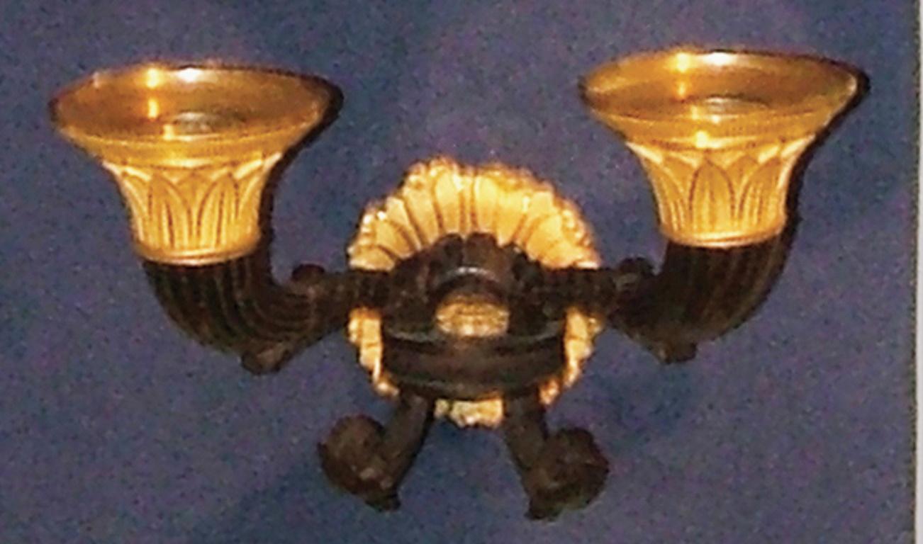 A set of four early 19th century French bronze and ormolu wall lights, having leaf decorated nozzles above scrolled acanthus and reeded candles-arms.