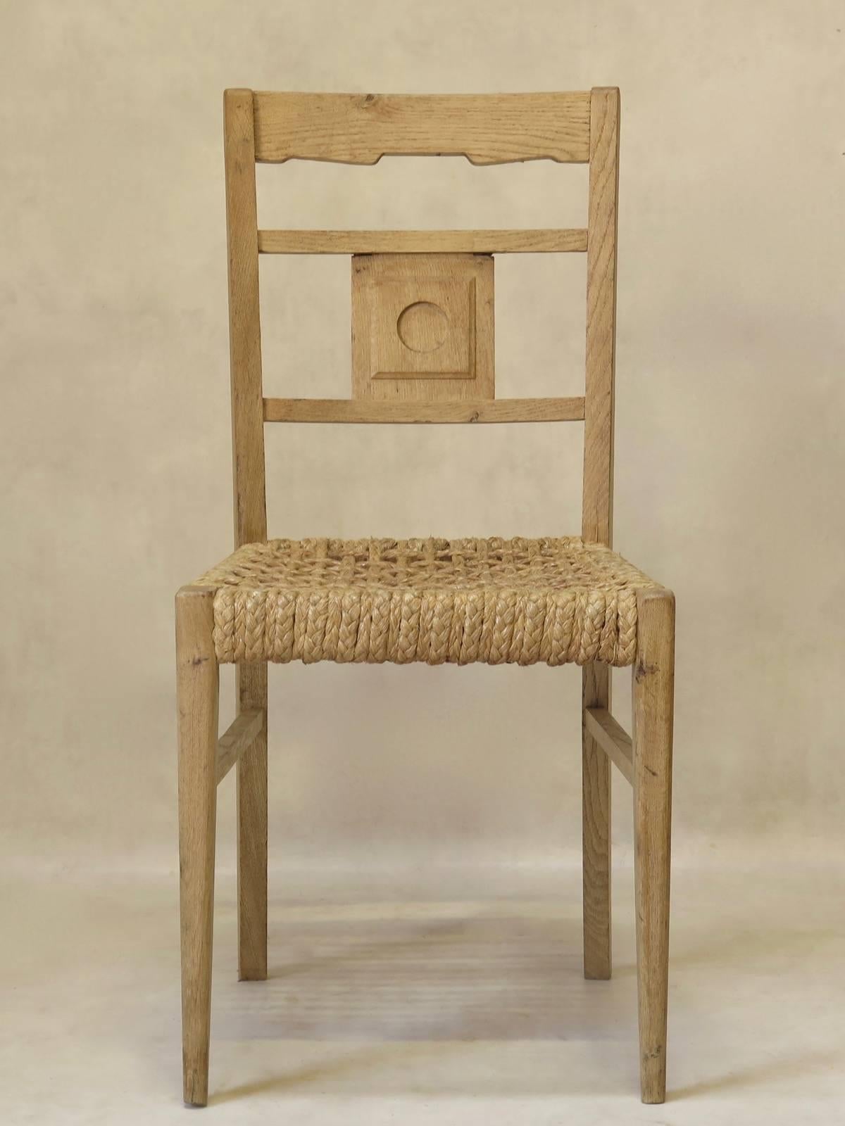 Chic and unfussy set of four oak dining chairs with rope seats, attributed to Adrien Audoux and Frida Minet, of Vibo Vesoul. The backs have a simple medallion decor. The front legs are tapered.