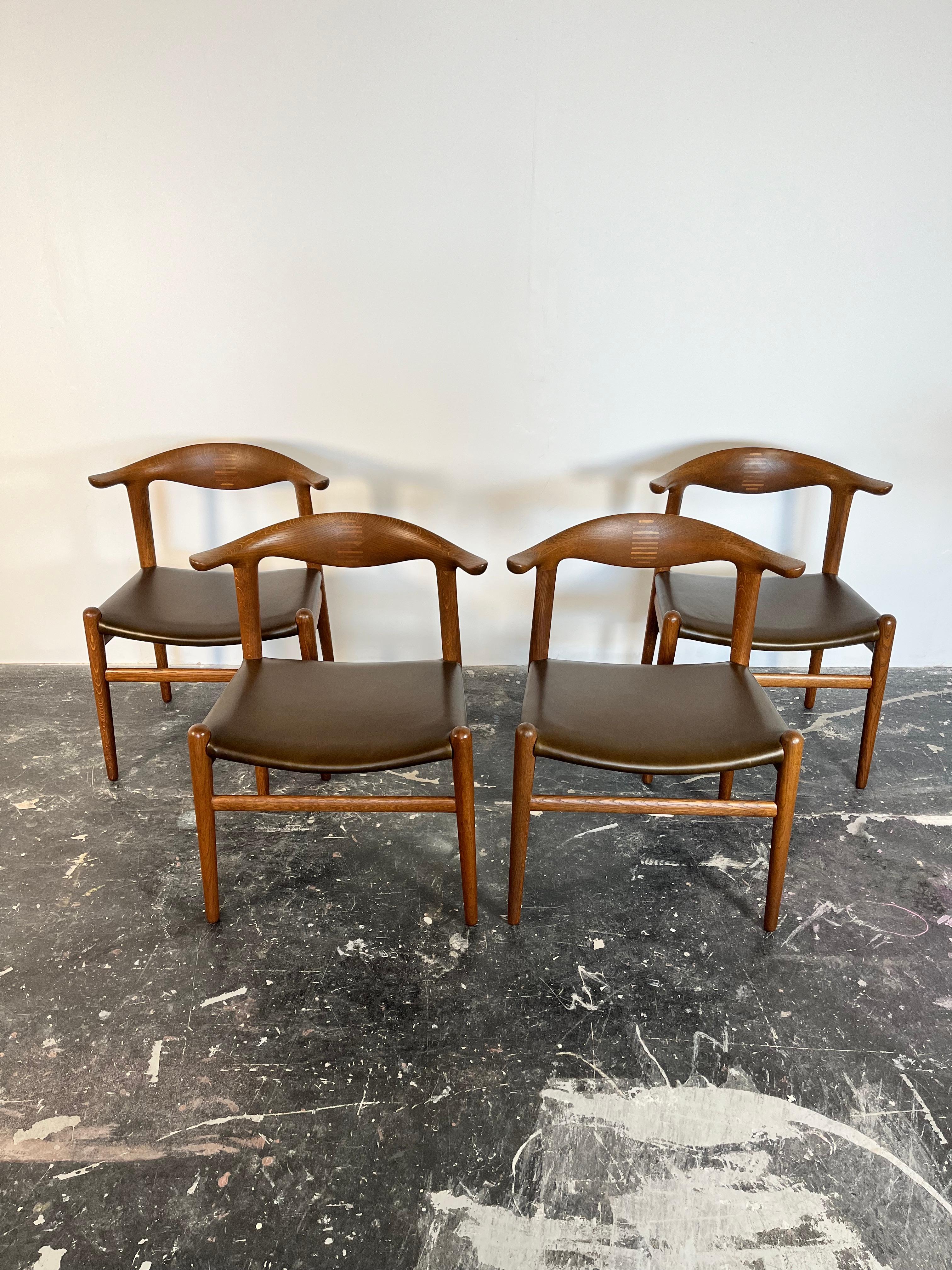 Set of 4 Restored Oak Cow Horn chairs by Hans Wegner with new olive green leather seats. 

This set of Cow Horn Chairs are rarely seen and extraordinarily crafted with inlays of Brazilian rosewood which lock the back joint. Metal tags on chair show