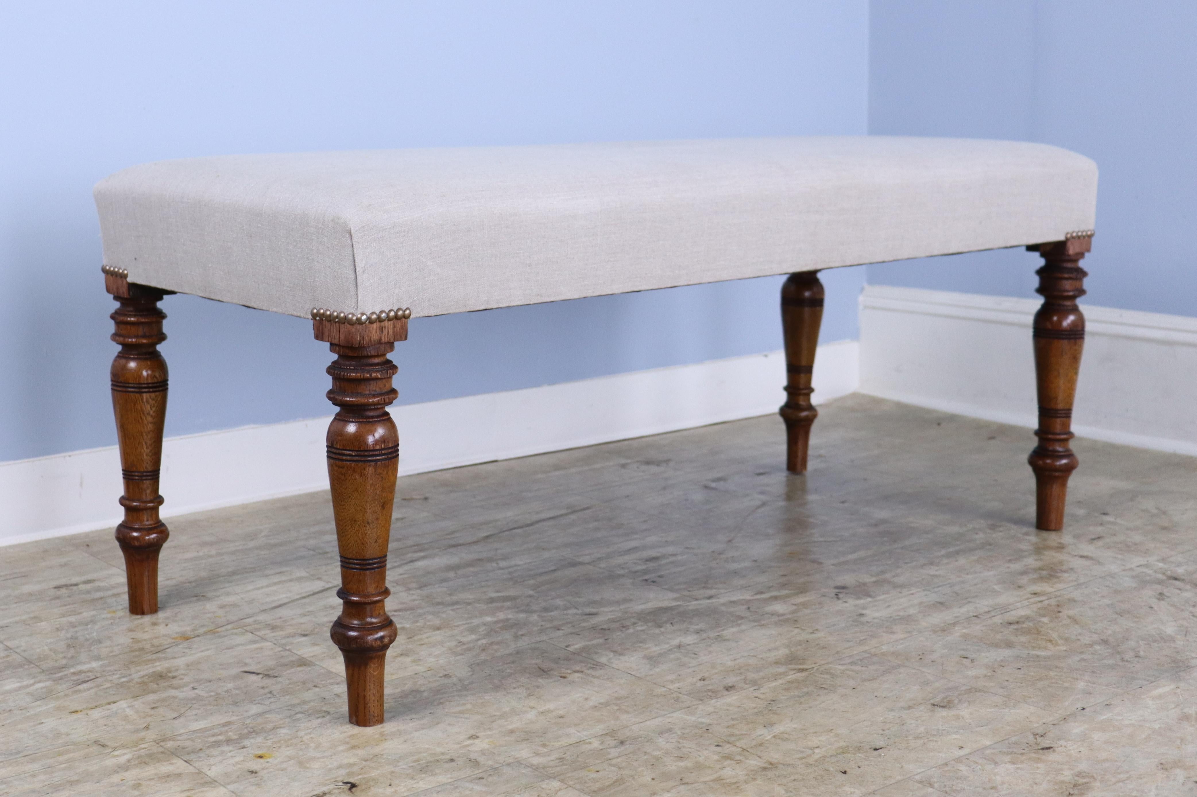 An elegant stool newly covered in French beige linen, with decorative nailheads at the edge of the seat. Constructed with mahogany legs, circa 1890 that are well-carved and sturdy. Very good sitting-height, comfortable seating at the end of the bed.