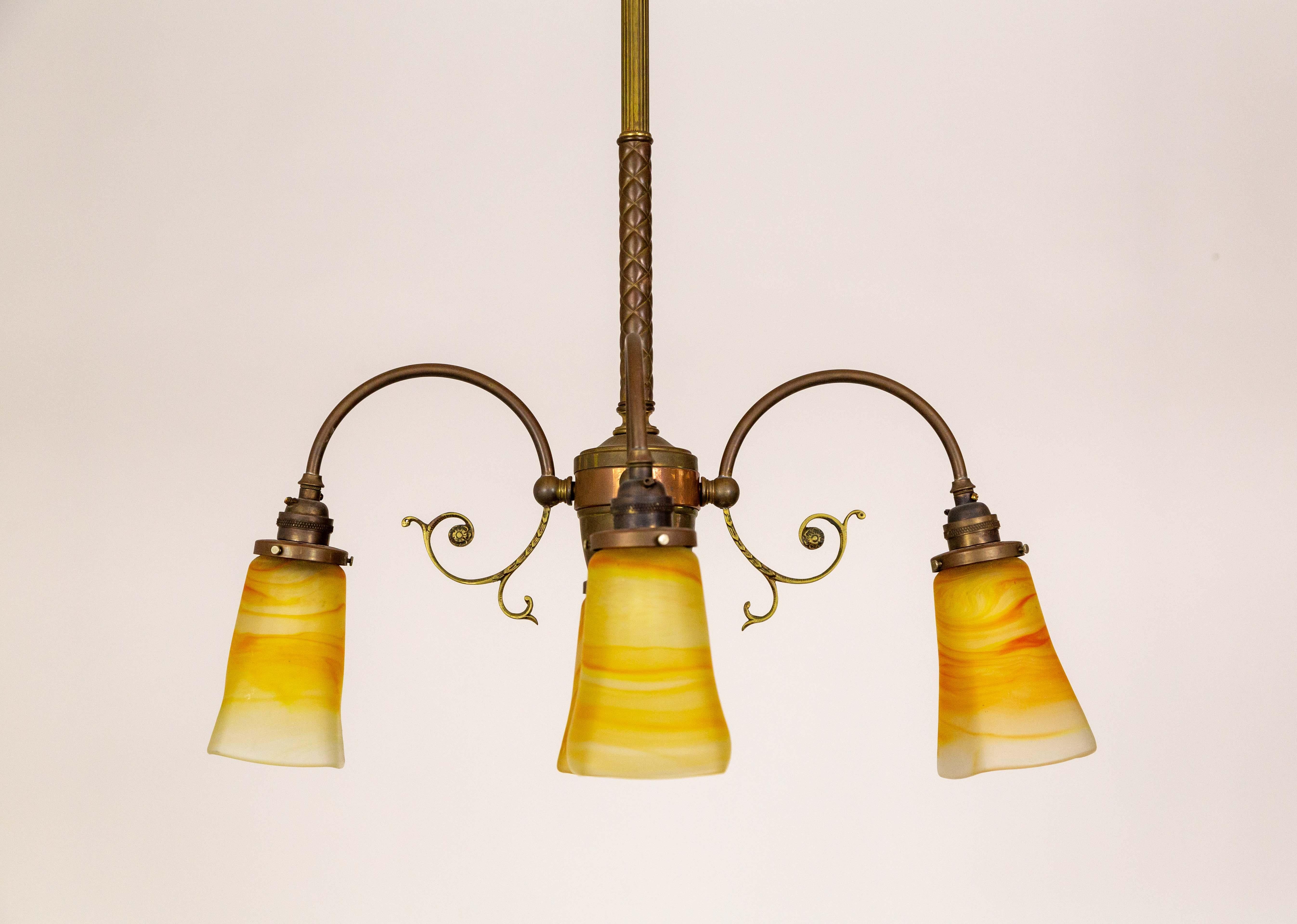 A chandelier with 4 downlights and yellow-orange streaked frosted glass shades, made by Vianne in France. It has a patinated brass structure with a copper rim on the body, downward, C-curve arms, and a cast reeded and quilted stem. Newly rewired.