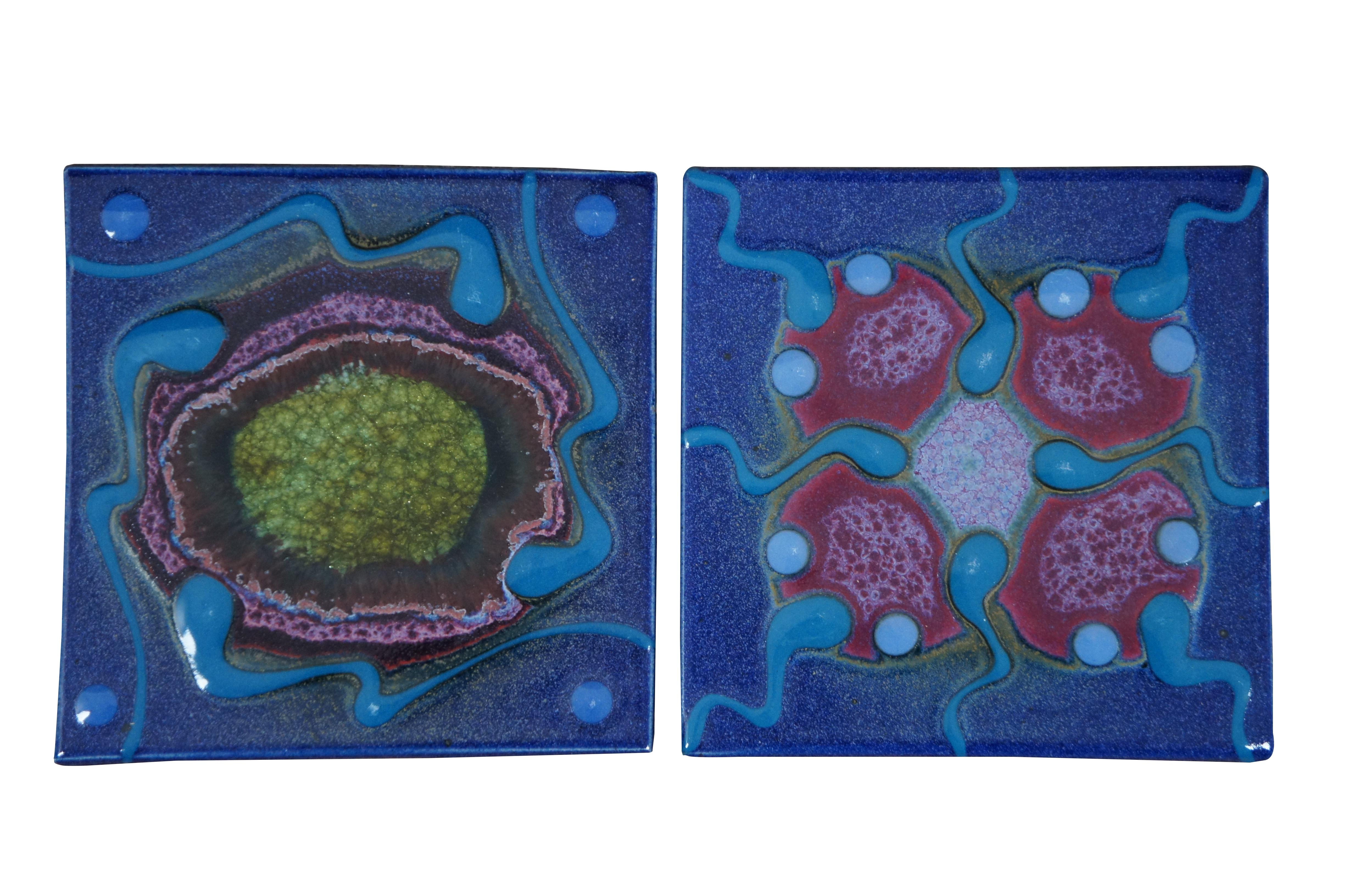 Set of four late 20th century ceramic art pottery tiles / trivets / hot pads by Matthew Patton of Orcas Island Pottery. Set includes two larger and two smaller tiles with cork pads underneath, and feature four designs in blue, green, red, and