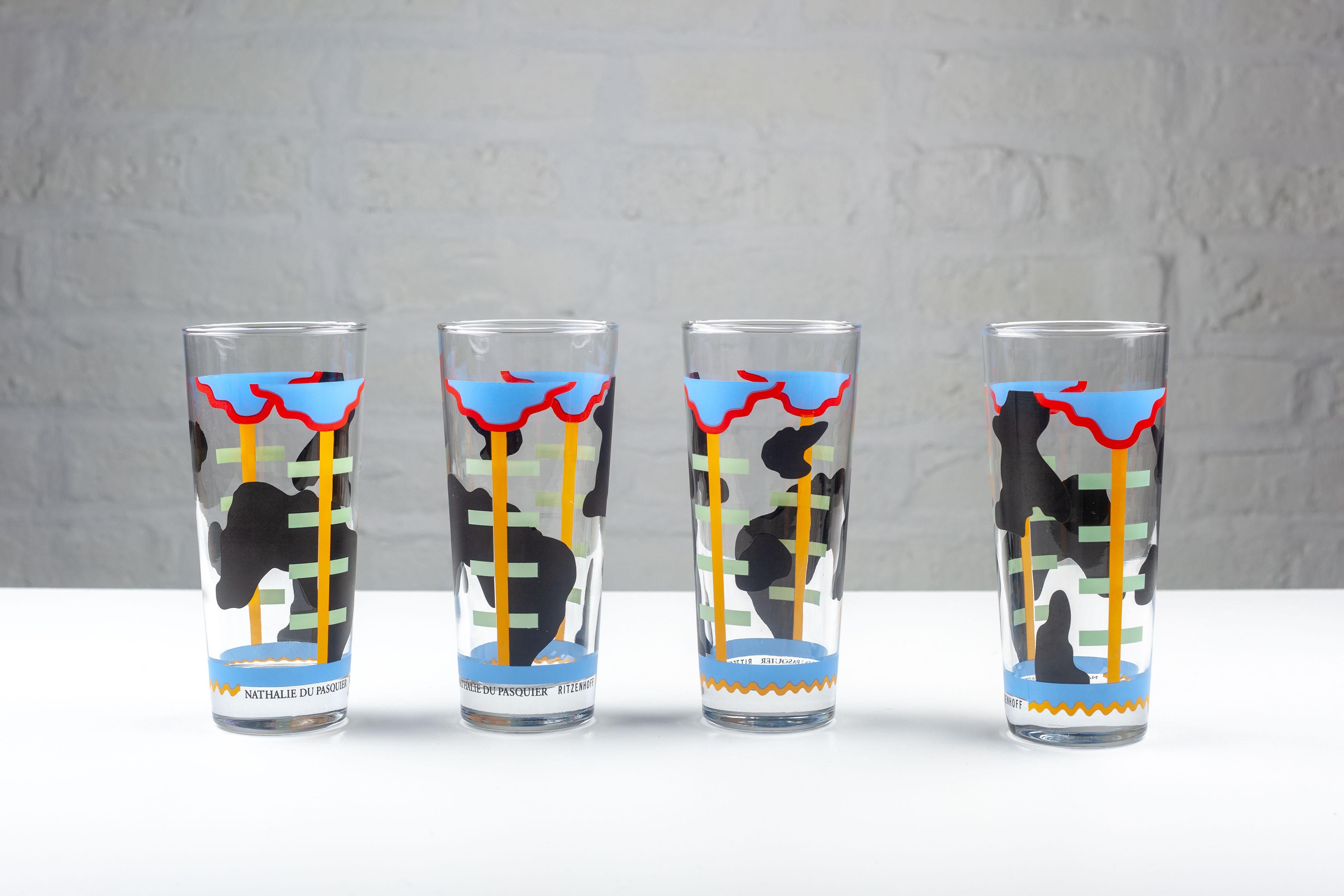 Set of four Memphis glasses, each adorned with a unique, abstract design by Nathalie du Pasquier for Ritzenhoff. They feature a distinctive style characterized by bold colors and geometric patterns. The central theme appears to be a stylized