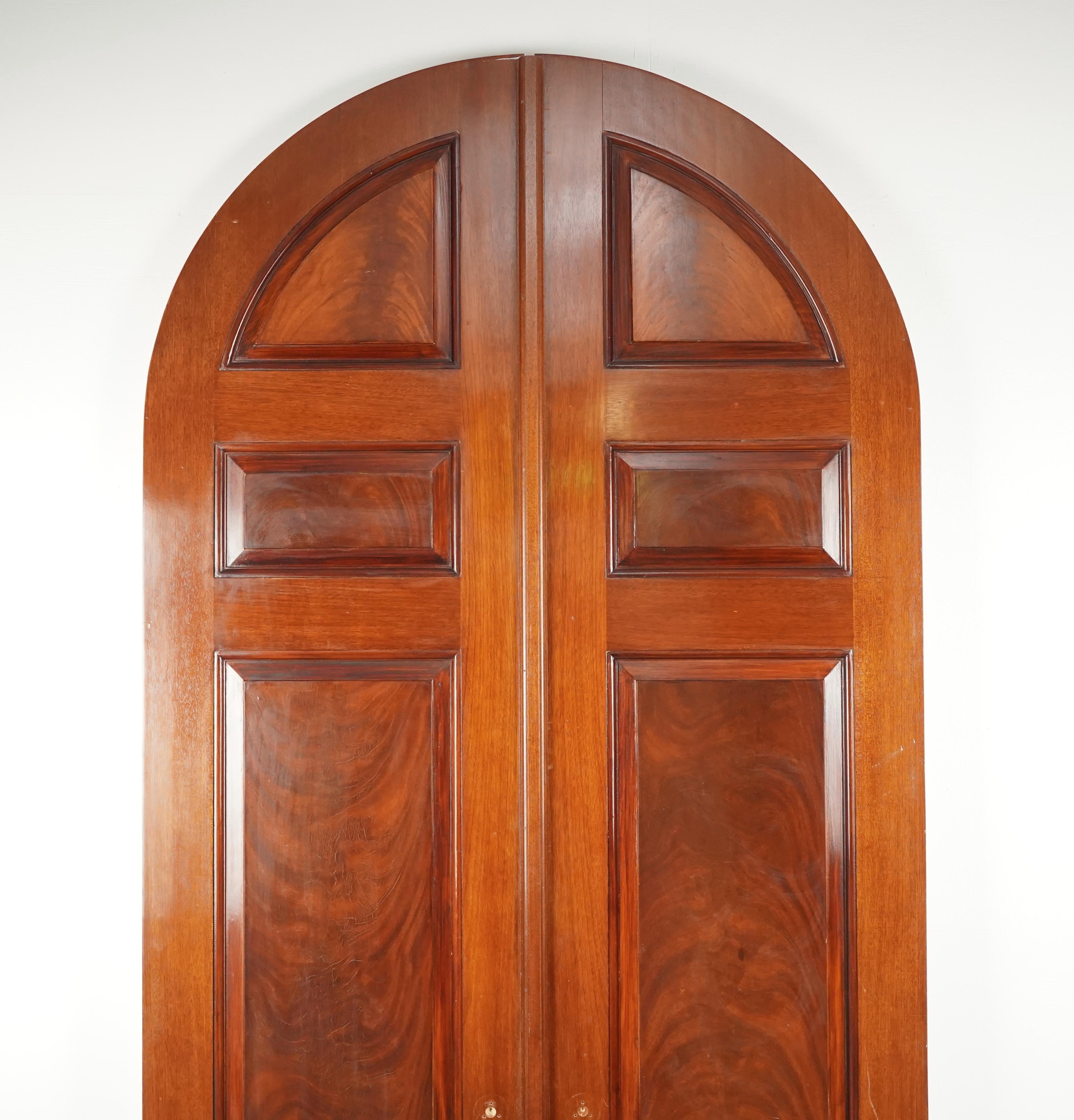 20th Century in swing arched double doors made of walnut and mahogany with a dark stain on one side and painted white on the other. Each door has four panels. The doors are in good solid condition with surface wear. Please refer to the pictures for