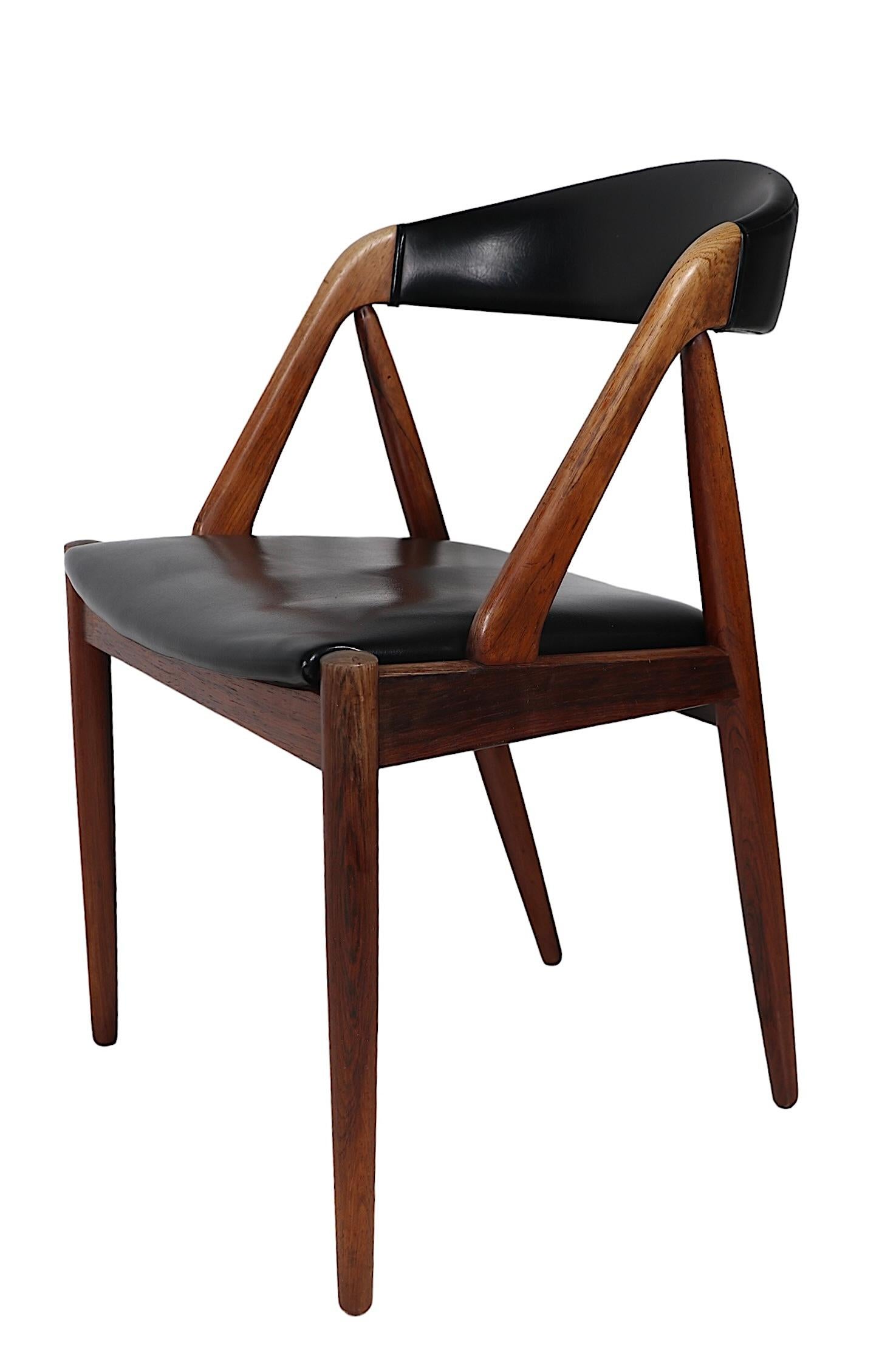 Iconic Danish Mid Century Modern dining chairs designed by Kai Kristiansen, made in Denmark by Shou Andersen Mobelfabrik, circa 1960's. The chairs feature  sculptural, architectural frames of solid rosewood, with graphic black vinyl seats and backs.