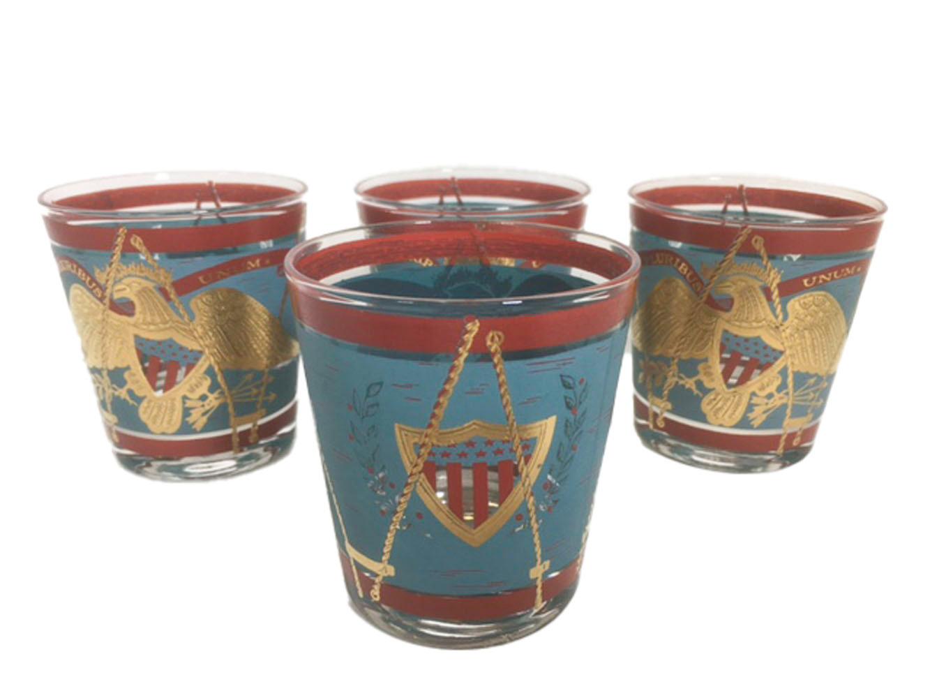 Mid-Century Modern old fashioned glasses decorated as parade drums in teal and red enamel with 22 karat gold.
The front with a large patriotic eagle below a banner with the motto E Pluribus Unum. The eagle with a stars and stripes shield on its