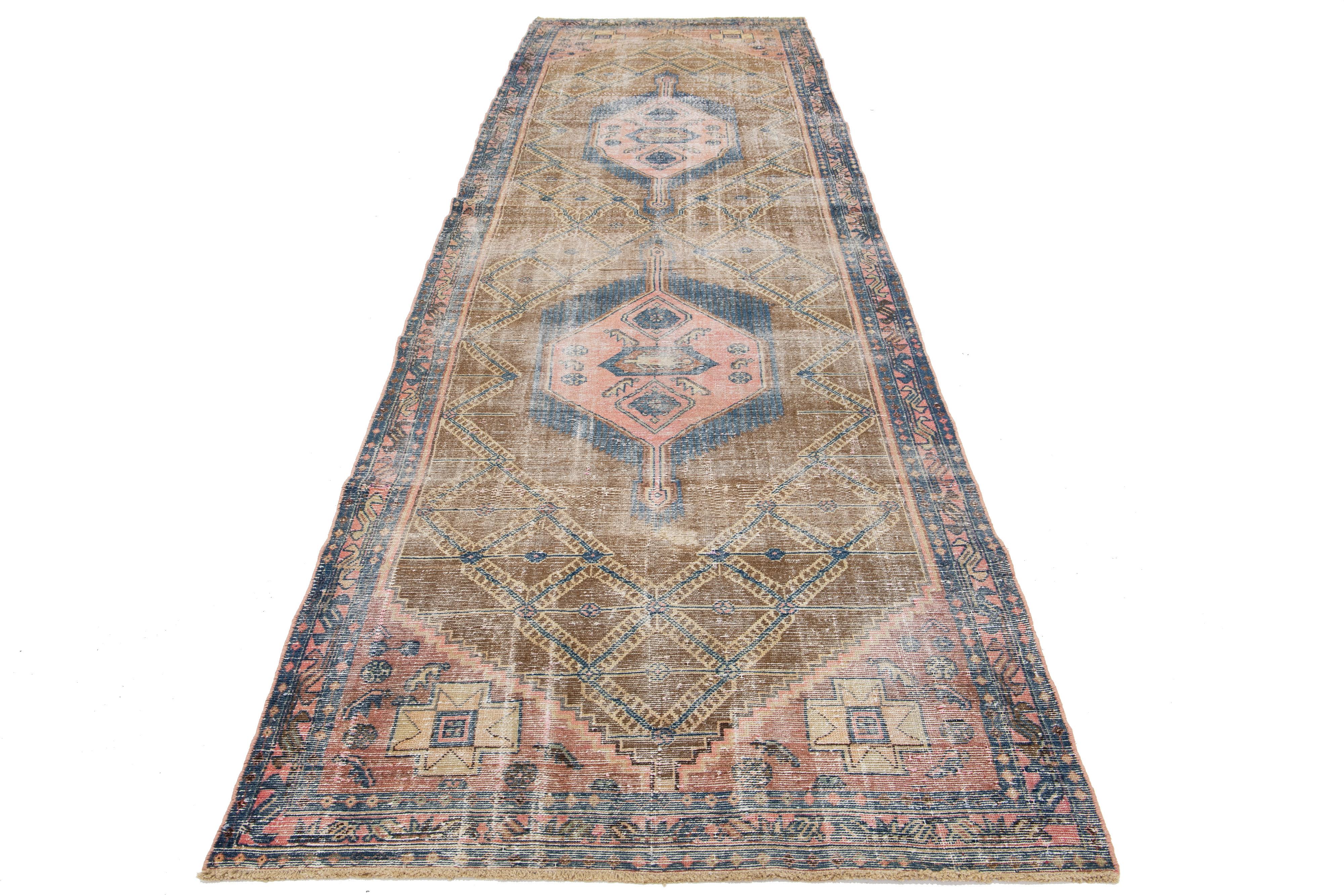 Dieser Läufer aus Vintage-Wolle zeigt ein braunes Feld mit pfirsichfarbenen und blauen Stammesakzenten persischen Ursprungs.

Dieser Teppich misst 4'2