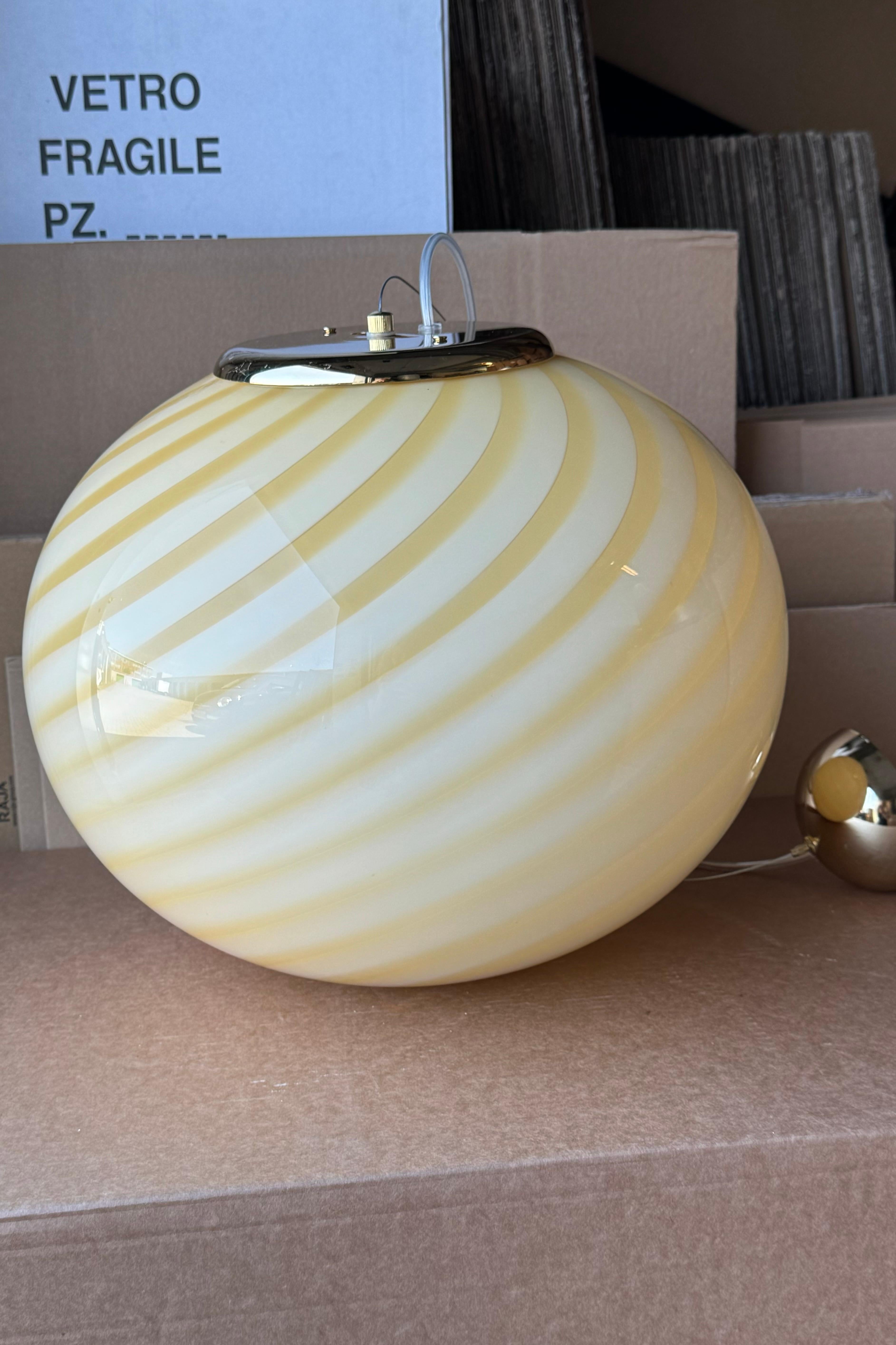 Large new Italian Murano candy pendant ceiling lamp in a beautiful soft yellow shade. Mouth-blown glass in oval shape with swirl pattern. E27 socket. Comes with adjustable brass or chrome plated suspension as well as transparent cord.
Handmade in