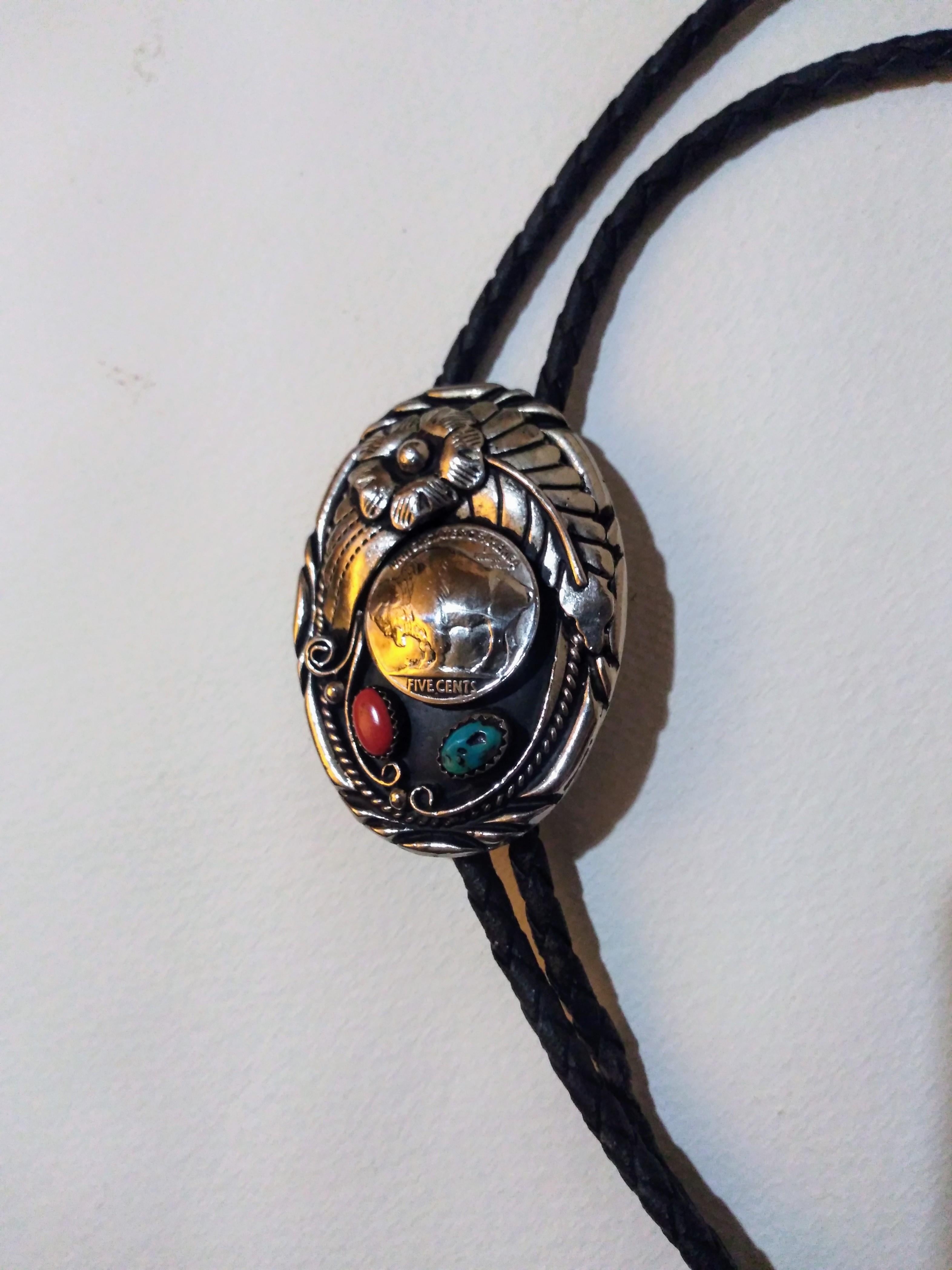 This is a beautiful bolo tie. It's made of braided leather with a sterling silver medallion that has a turquoise and a coral setting. The tips are crafted in silver also.

Great for a night out on the town.


Ready to wear.