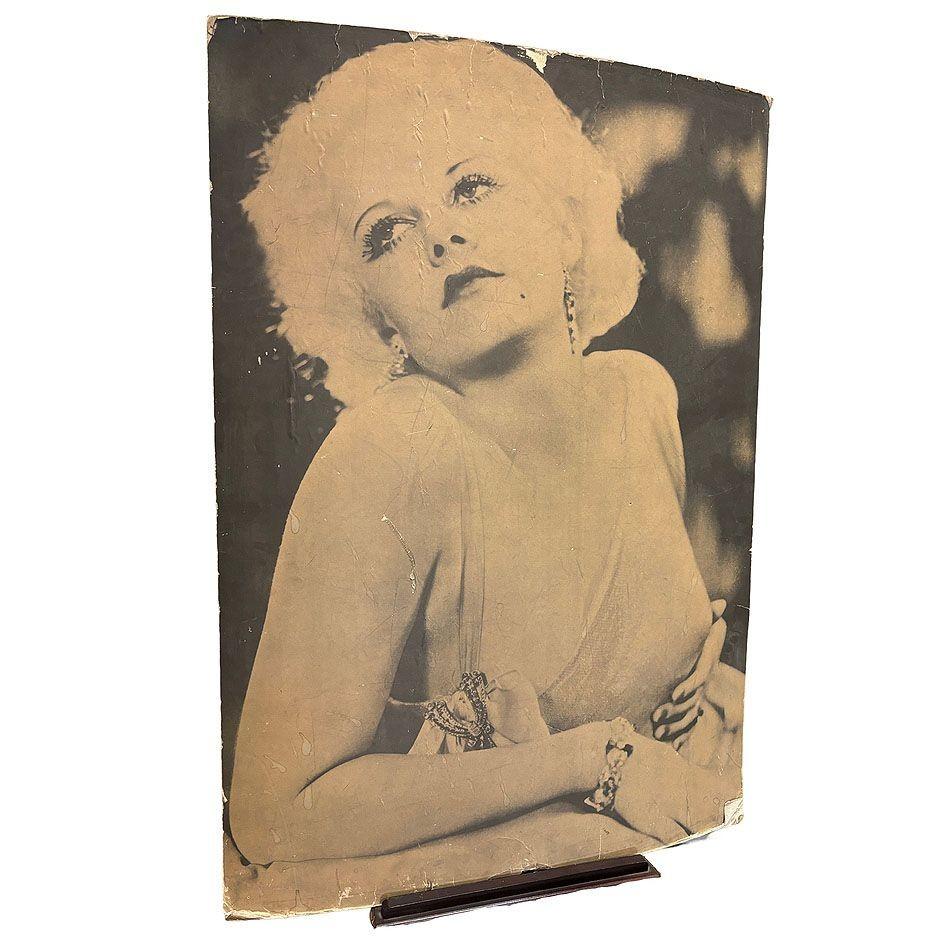 This glamorous 1950s matte poster-size photograph captures Hollywood icon Jean Harlow in an alluring yet tasteful pose. She gazes upward with a dreamy expression, her signature platinum blonde curls framing her face. Her exposed shoulder adds a hint
