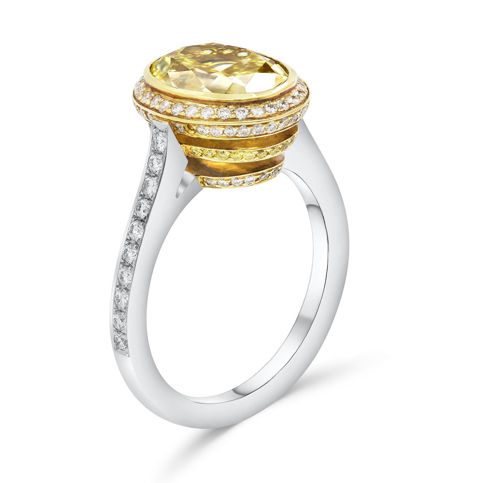 This elegant engagement ring features a color-rich yellow oval cut diamond center that GIA certified as Fancy Intense Yellow color. The diamond is bezel set in 18 karat yellow gold basket accented by a single row of sparkling round diamonds. The