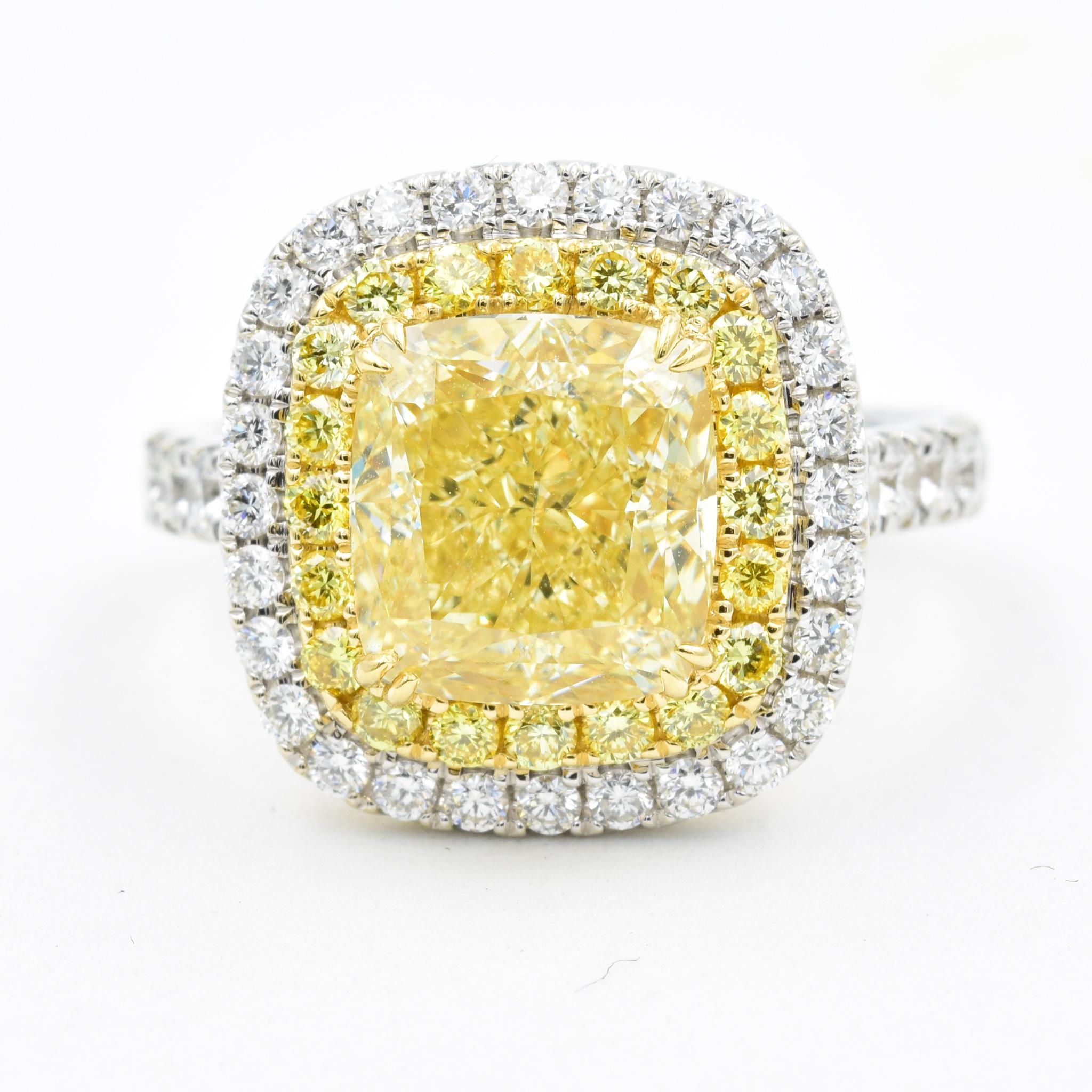 This gorgeous diamond ring features a GIA Certified cushion cut center diamond with fancy yellow color.  The diamond double-halo features two rows of diamonds with the inner row being fancy yellow.  The side of the ring features round brilliant cut