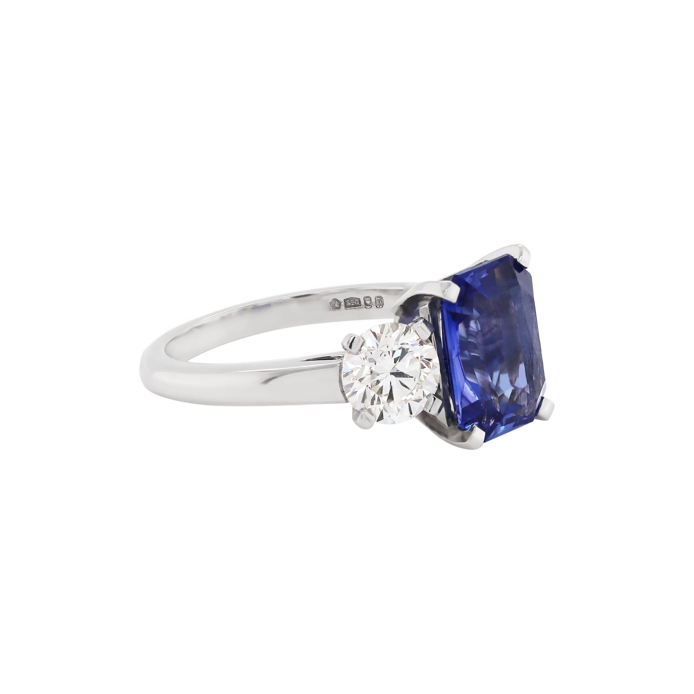 Beautiful handmade engagement ring set with a certified natural unheated transparent blue rectangular cut sapphire weighing a total of 4.02 carats mounted in a four claw, open back setting, accompanied by two round brilliant cut diamonds, one on