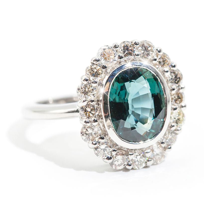Forged in platinum, this vintage inspired halo ring features an alluring unheated 4.02 carat oval natural colour shifting green blue sapphire complimented by a carefully set scalloped border of 1.18 carats of sparkling round brilliant cut diamonds.