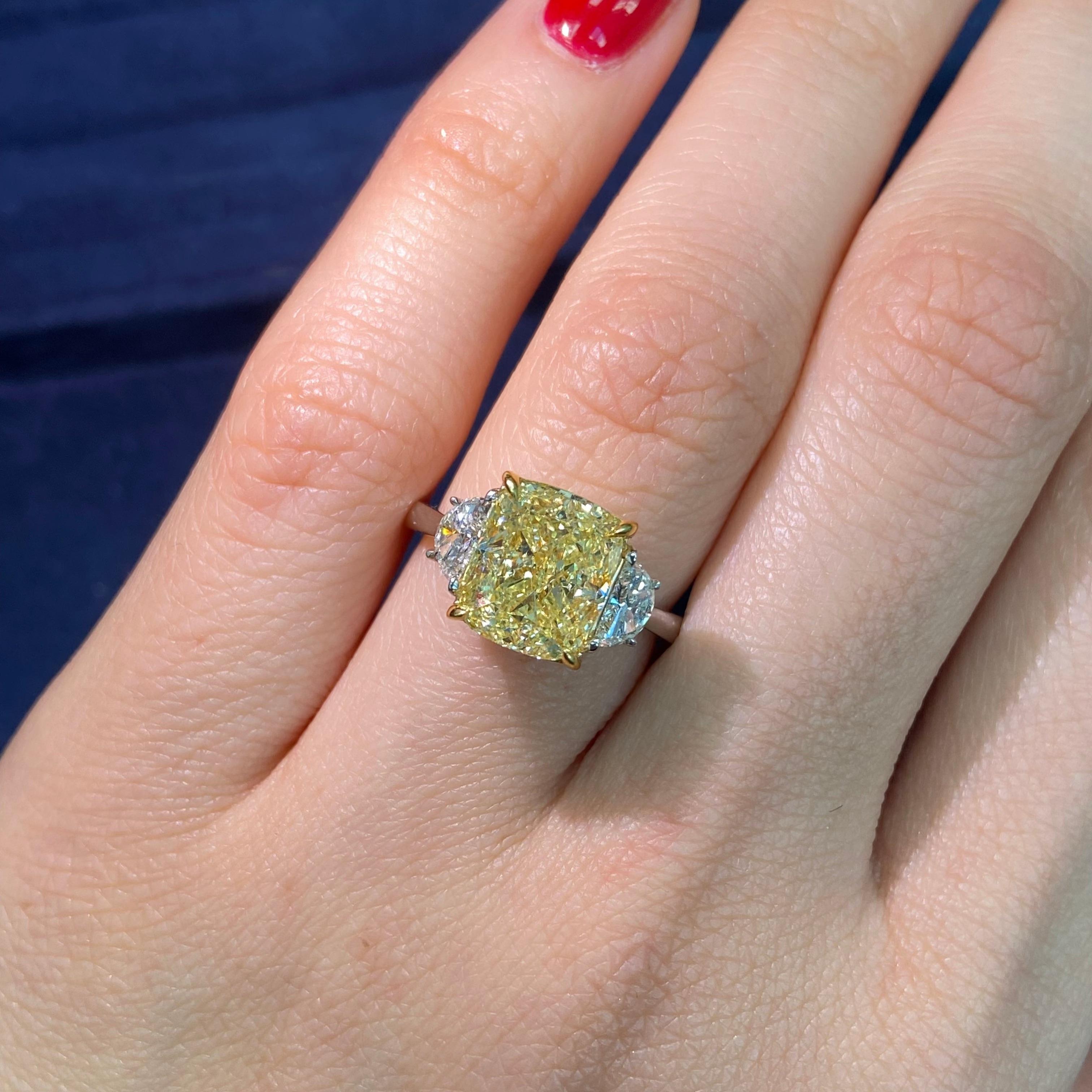 This 4.02-carat Fancy Yellow three-stone engagement ring is a stunning example of timeless elegance and meaningful design. Featuring a cushion-cut Fancy Yellow diamond at its center, flanked by two white trapezoid diamonds, the ring achieves a