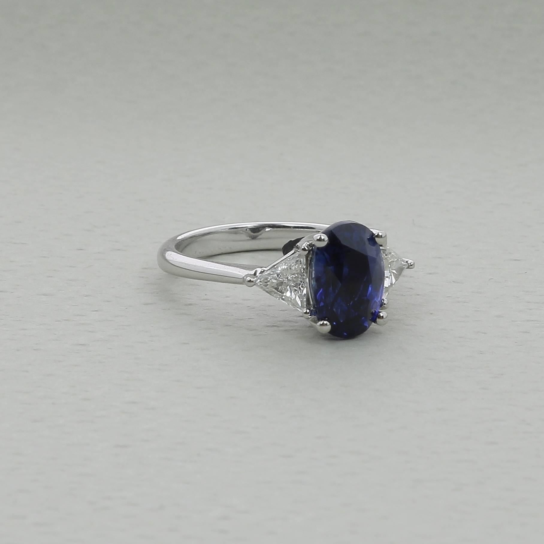 A Blue Sapphire Ring weighing 4.03 carats. 
The stone’s shape is oval, having for colors a striking Blue. 
The ring is set on each side by a single trillion-cut diamond (also called “trilliant-cut-diamond” or “trillian-cut-diamond”) weighing 0.49