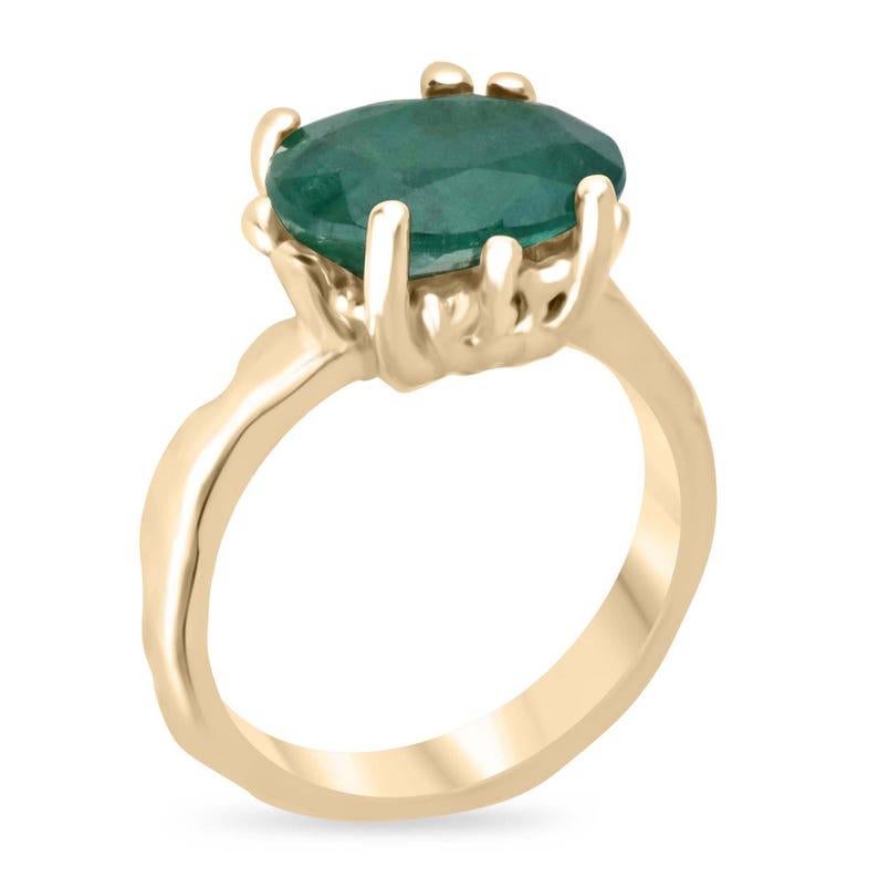 This captivating solitaire ring features an oval-cut Zambian emerald, boasting a dark green color with semi-transparent clarity. Set in a fun, organic gold design, the intricate prongs and gold nugget-like band style add a unique, earthy charm.