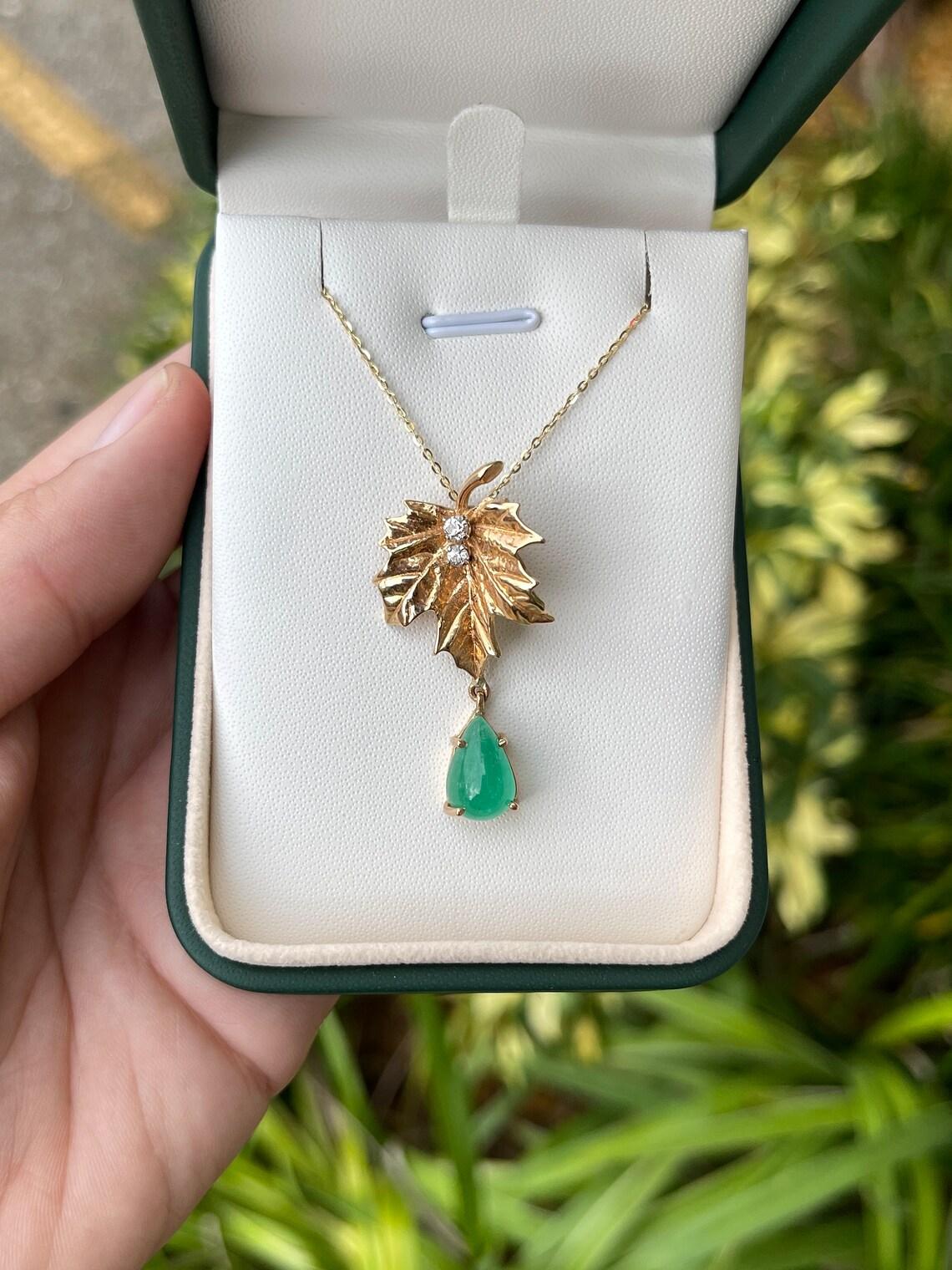 Displayed is a divine 4.05tcw natural unique Colombian emerald and diamond accent leaf pendant. This is quite an alluring piece with a beautiful rare emerald drop. A pear shape cabochon cut Colombian emerald is prong-set in 14K yellow gold