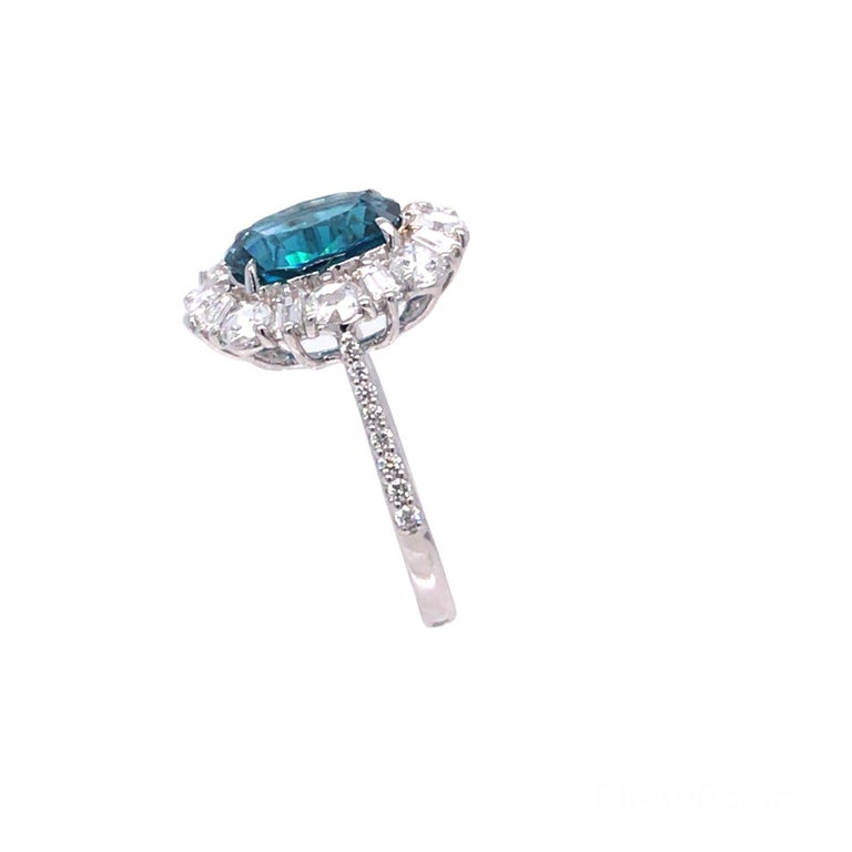 This ring has a 4.08 carat oval cut blue zircon center, surrounded by a halo of alternating round and baguette diamonds. Additional round diamonds decorate the shank. Set in 18k White Gold.

Center: 4.08 Carat Blue Zircon
Diamonds: Baguettes and