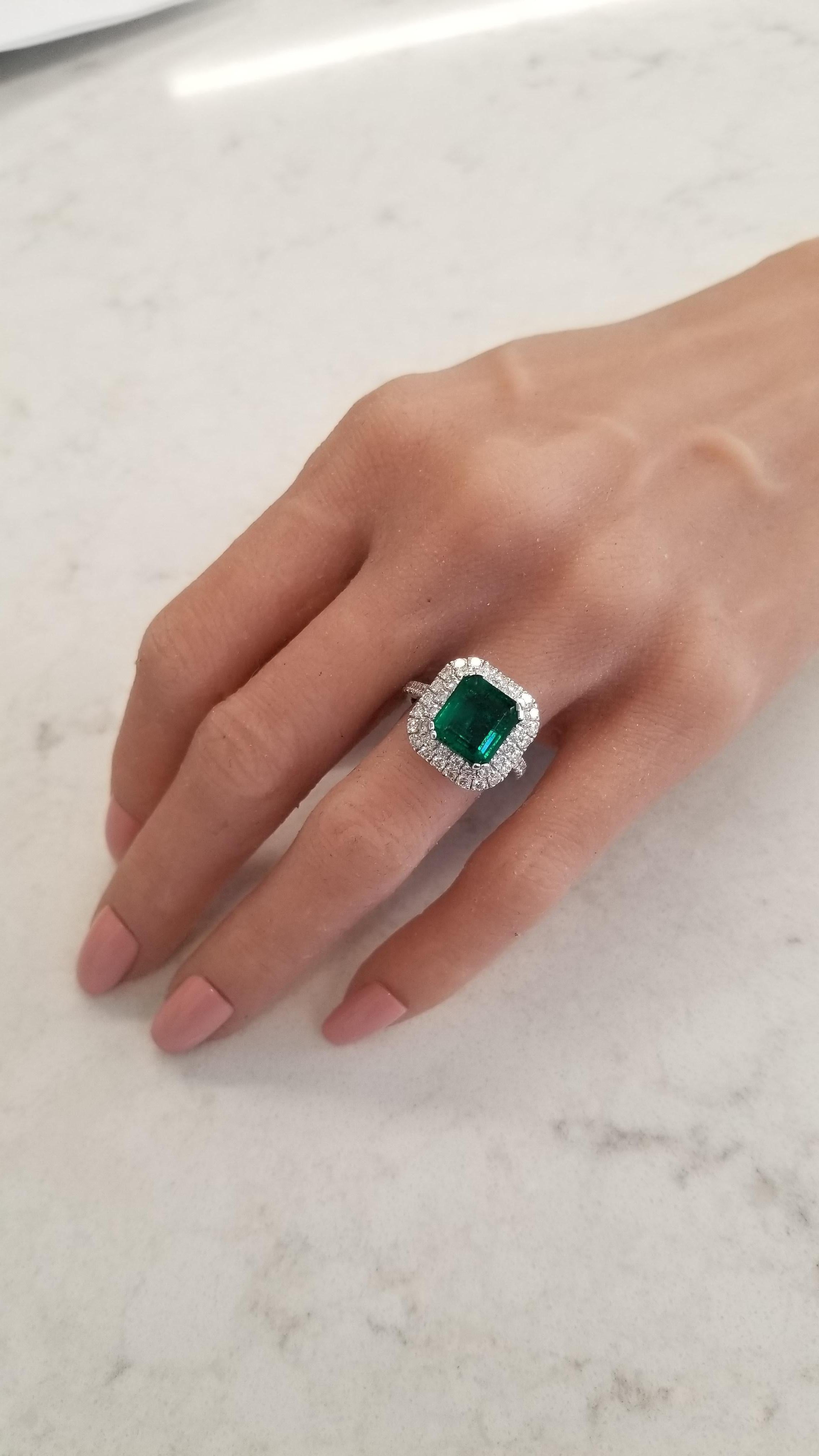 This is a 4.09 cushion cut intense green emerald that measures 10.10 x 9.10mm. The gem source is Colombia; its color is vibrant grass green. Its transparency and luster are excellent. Sparkling round brilliant cut diamonds frame this gem in a