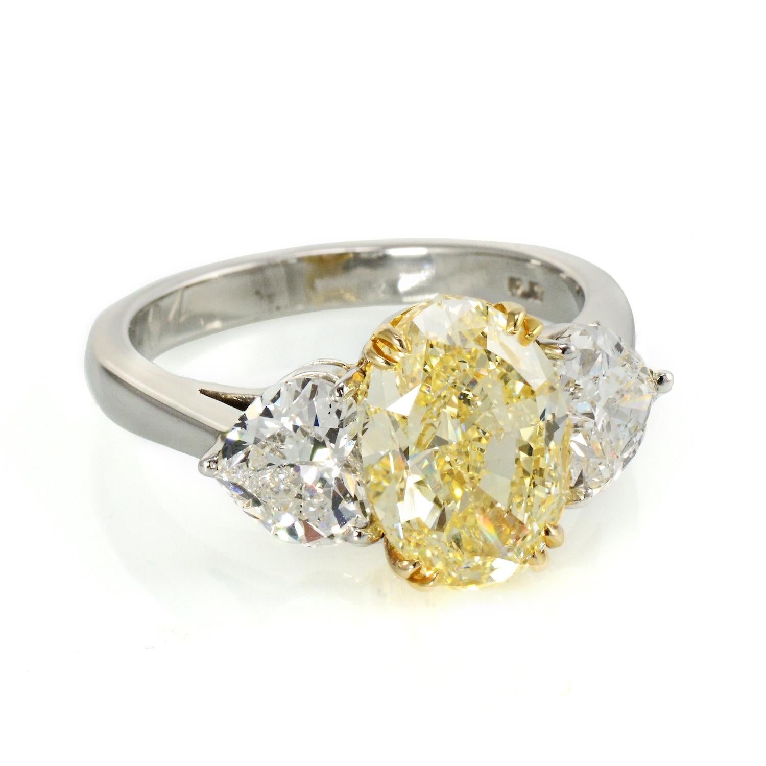 Immerse yourself in the timeless allure of this extraordinary three-stone engagement ring, a true embodiment of sophistication and style. At its heart, a dazzling 4.09-carat Natural Fancy Light Yellow Oval Cut diamond takes center stage, exuding a