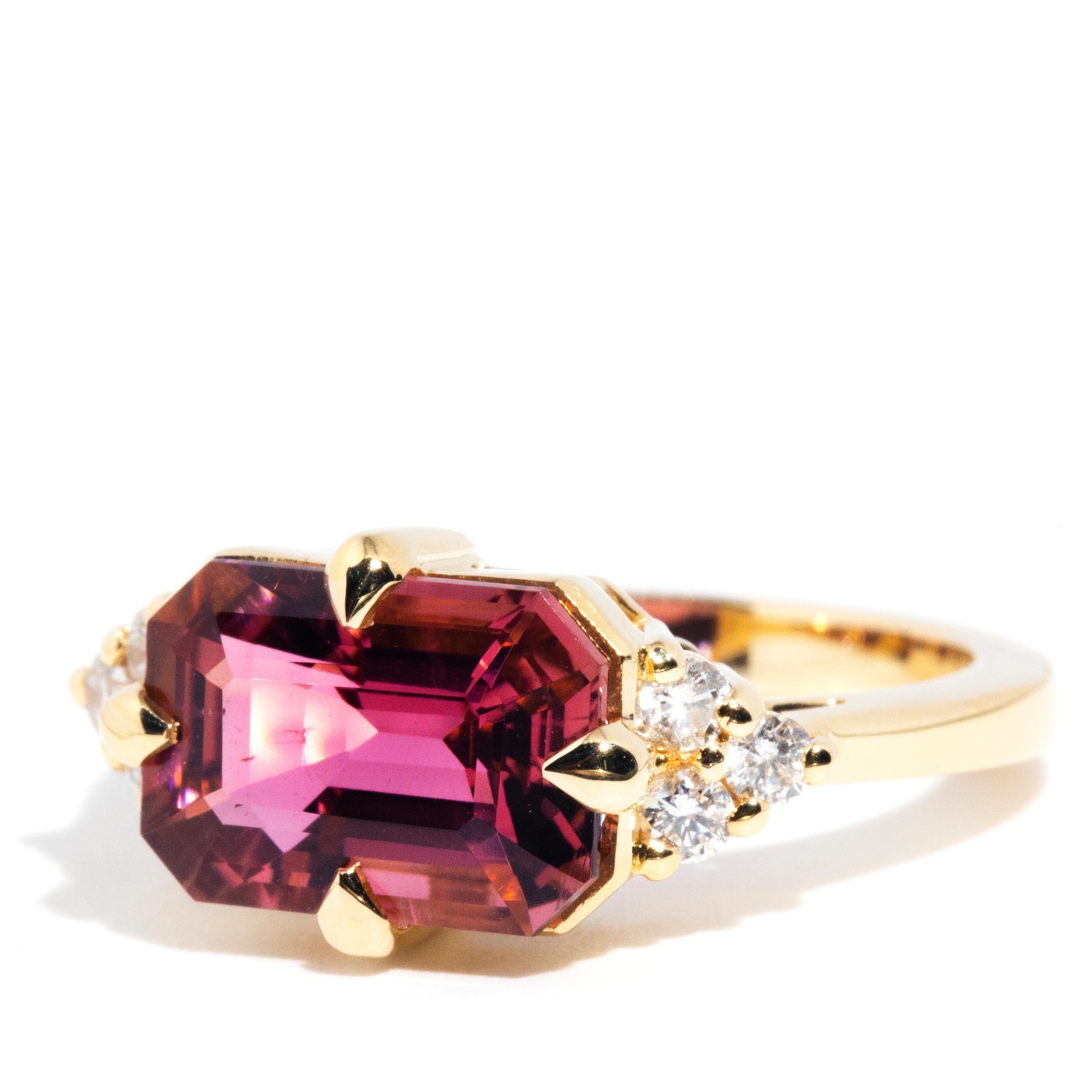 Forged in 18 carat yellow gold, this uniquely designed contemporary ring is absolutely gorgeous holding a captivating 4.09 carat bright reddish-pink emerald cut tourmaline flanked by a total of 0.30 carats of round brilliant cut diamonds arranged in