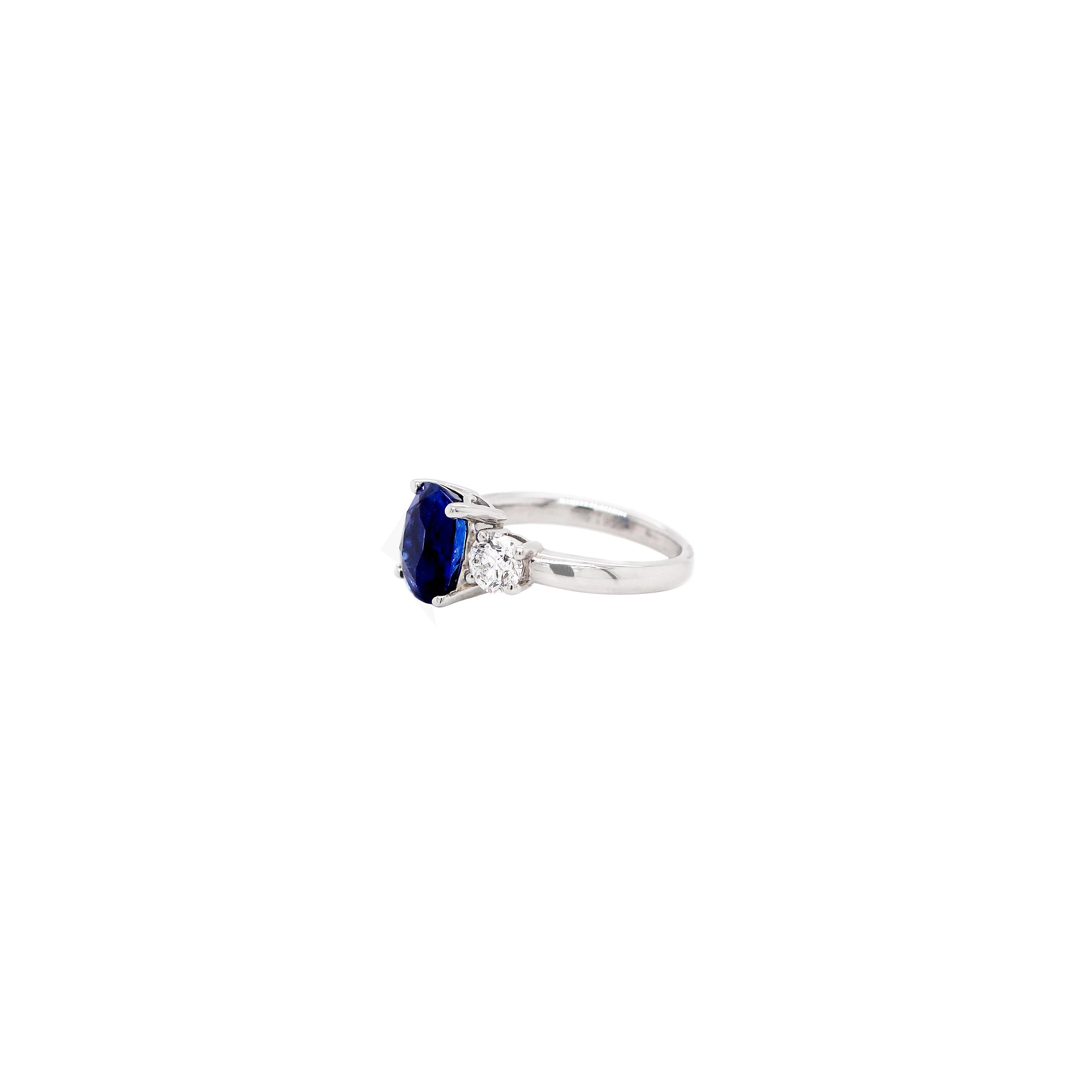 An exquisite three stone ring featuring a beautiful cushion shaped royal blue sapphire weighing 4.09ct in an open back, four claw setting. This gorgeous stone is accompanied by two certified D SI2 round brilliant cut diamonds on either side weighing