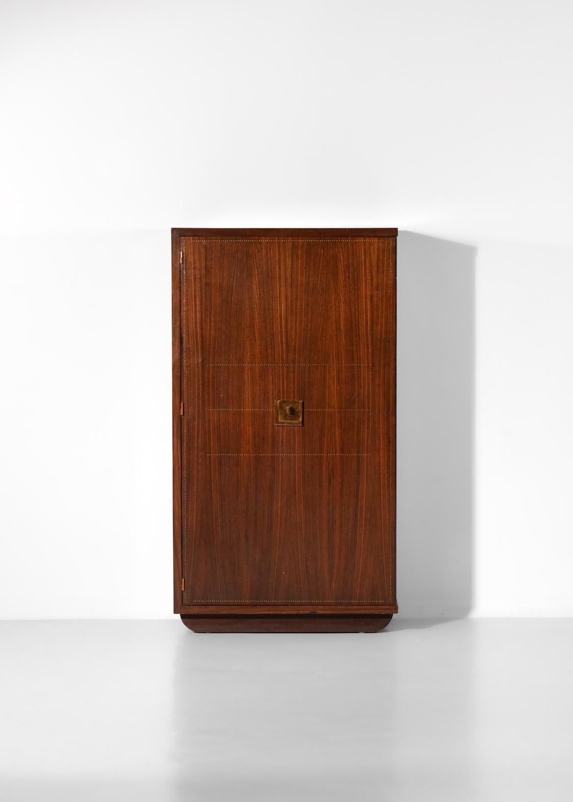 1940s cabinet by French designer André Sornay. The structure is made of solid mahogany and veneered wood, highlighted by a system of brass nails perfectly aligned around the edges of the furniture (see photos). The large door opens onto a series of