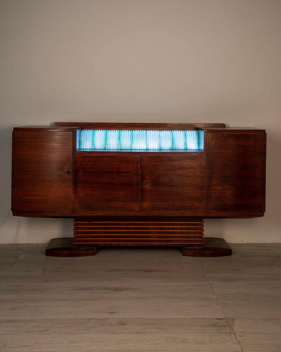 Sideboard in walnut veneered wood with four doors with lock and keys; built-in lamp on the upper floor with worked glass lampshade, 1940s, Art Decò.

Condition: In good condition, it shows signs of wear due to time and small restoration works, the
