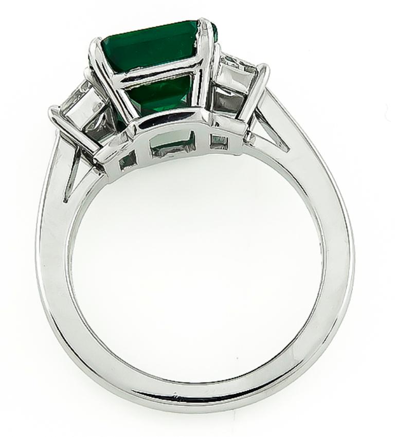 This fabulous platinum engagement ring is centered with a lovely emerald cut emerald that weighs 4.10ct. The emerald is accentuated by sparkling trapezoid cut diamonds that weigh approximately 0.90ct. graded H color with VS clarity. The ring is