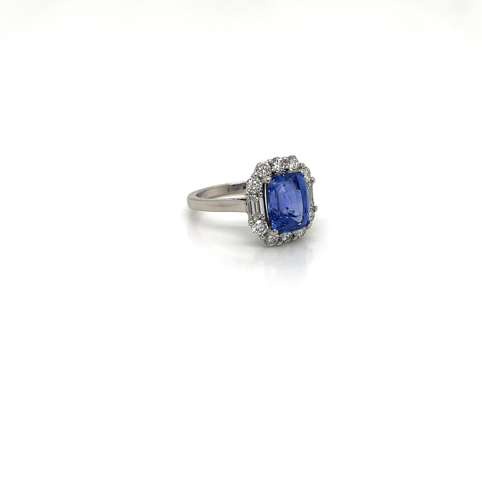 This striking ring features a flawless Oblong Cushion cut Blue Sapphire weighing 4.10 Carats at its centre with a unique arrangement of trapezoid and round brilliant diamonds surrounding it. The evident clarity of the alluring crystal clear blue