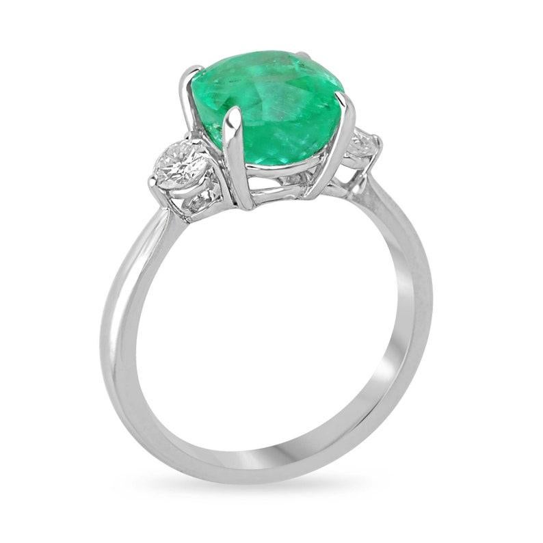 Découvrez une élégance inégalée avec notre bague à trois pierres en émeraude de Colombie et diamant. Une fascinante émeraude de 3,65 carats, taillée en coussin et provenant des mines renommées de Colombie, occupe le devant de la scène, affichant une