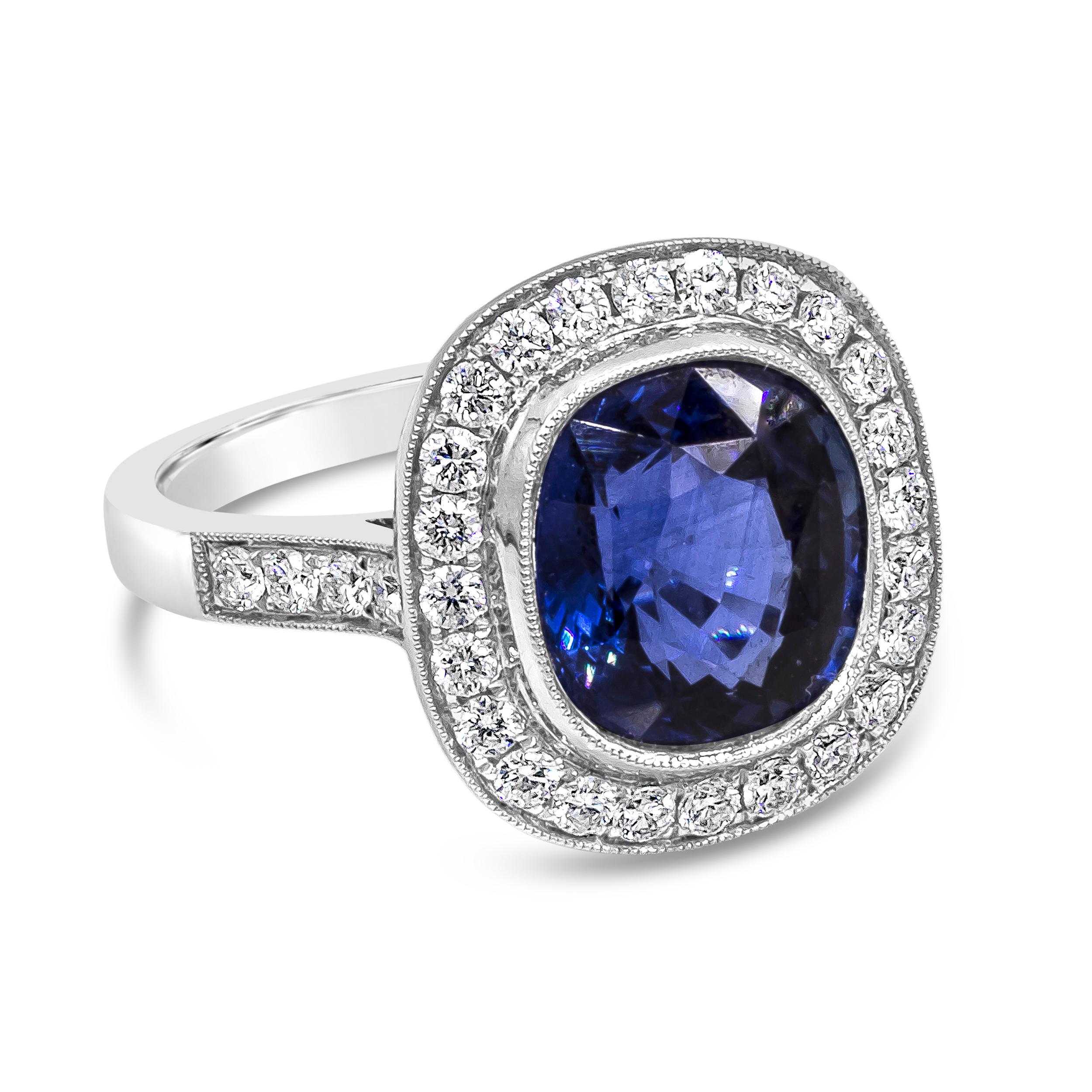 A vintage-style engagement ring showcasing a 4.12 carat cushion cut blue sapphire, surrounded by a single row of bezel-set halo round brilliant diamonds. Set in an 18K white gold mounting accented with diamonds. Finished with milgrain design on the