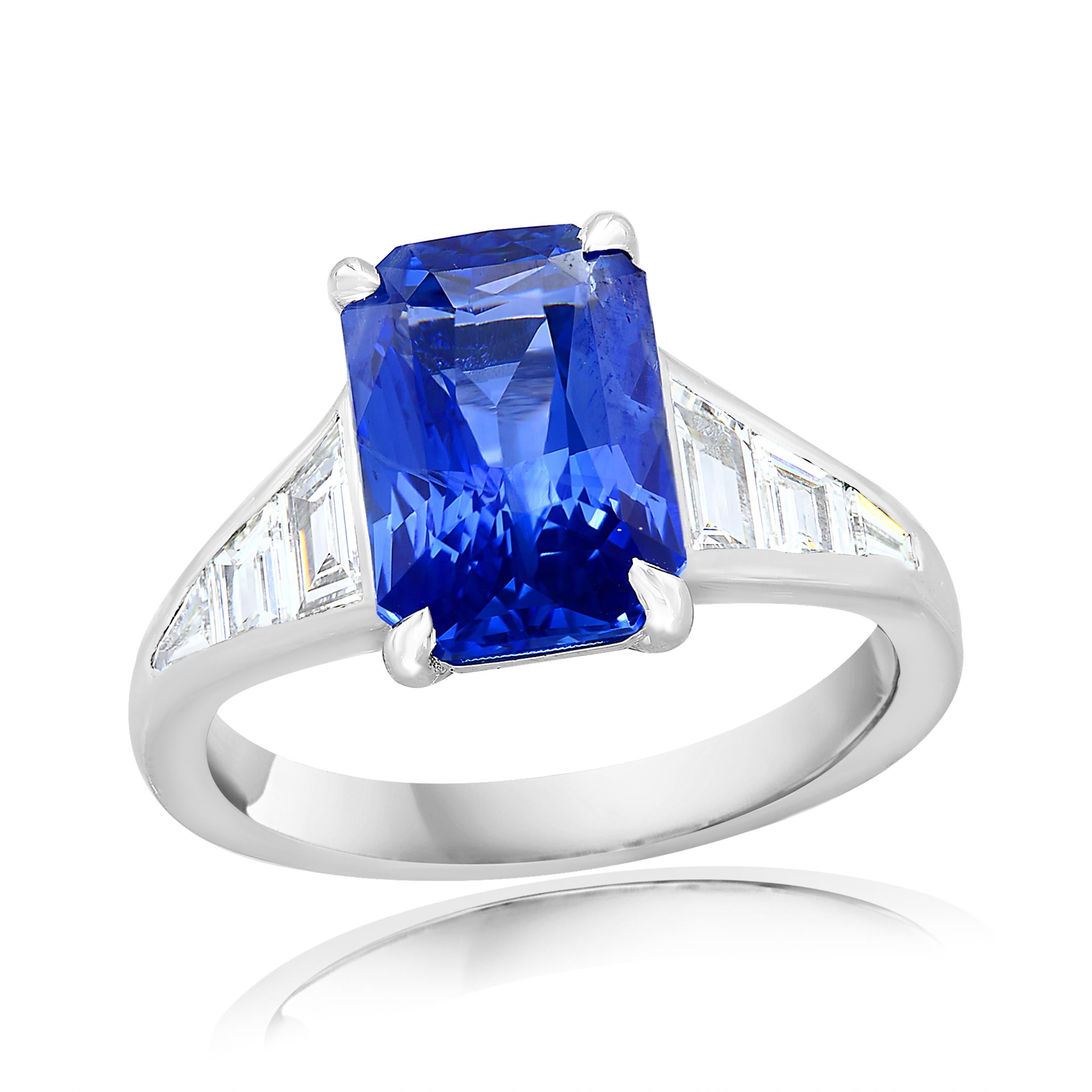 A stunning well-crafted engagement ring showcasing a 4.13-carat  emerald-cut Blue sapphire. Flanking the center diamond are perfectly matched graduating step-cut diamonds, channel set in a polished platinum mounting. 6 Accent diamonds weigh 0.65