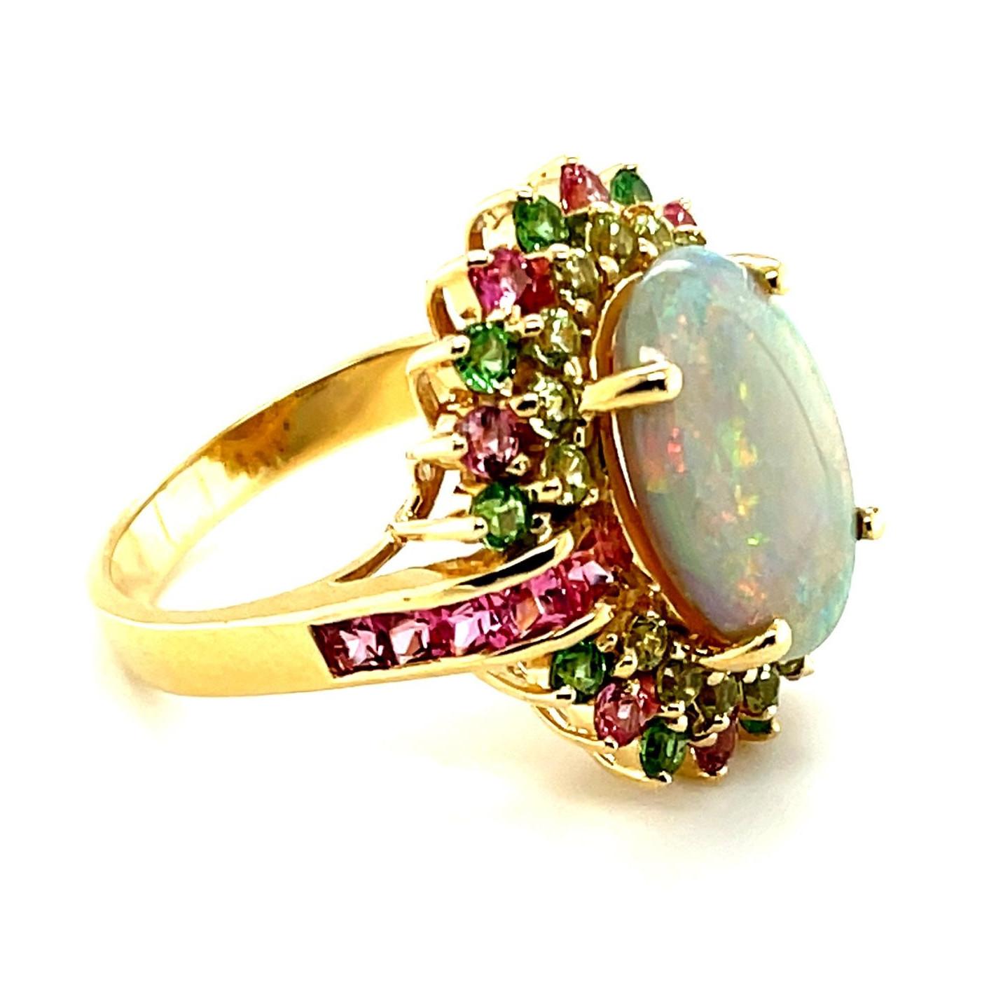 A beautiful, prismatic, 4.14 carat opal is central to this fun 14k yellow gold cocktail ring set with peridots, pink spinels and tsavorite garnets. Each of the gemstones chosen for this ring highlights this opal's fine play-of-color, making this