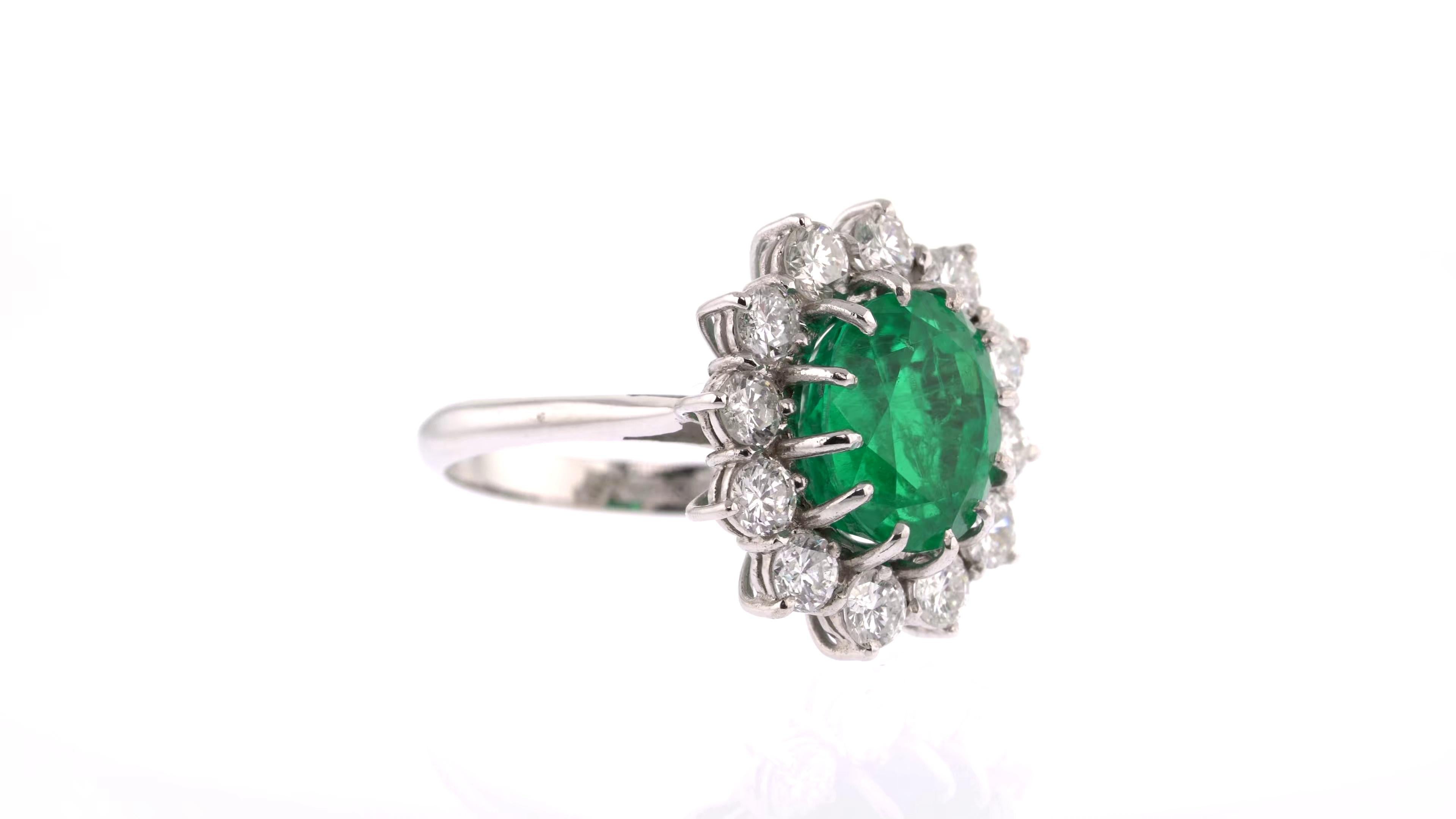 The vivid green emerald at the centre of this timeless piece ensures this is a ring that never will never go out of fashion. Its large size, classic oval shape and bright colour are emphasized by a sparkling halo surround of white round diamonds and