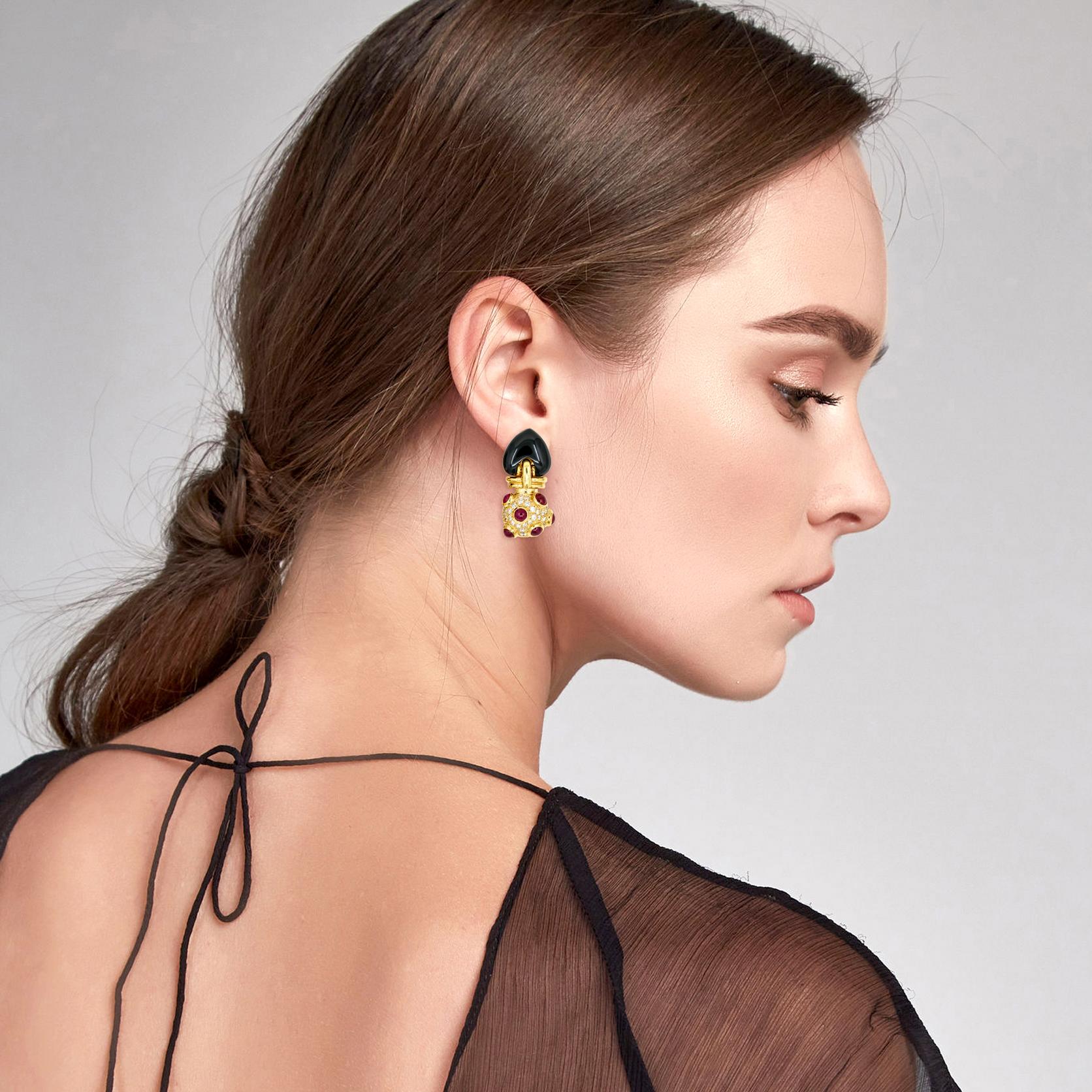 Onyx, Ruby and Diamond drop earrings in 18-karat yellow gold. Each earring has a large custom cut black onyx, bezel set with 6 cabochon natural rubies, and prong set with numerous near colorless brilliant round diamonds. Omega backs. Diamond color