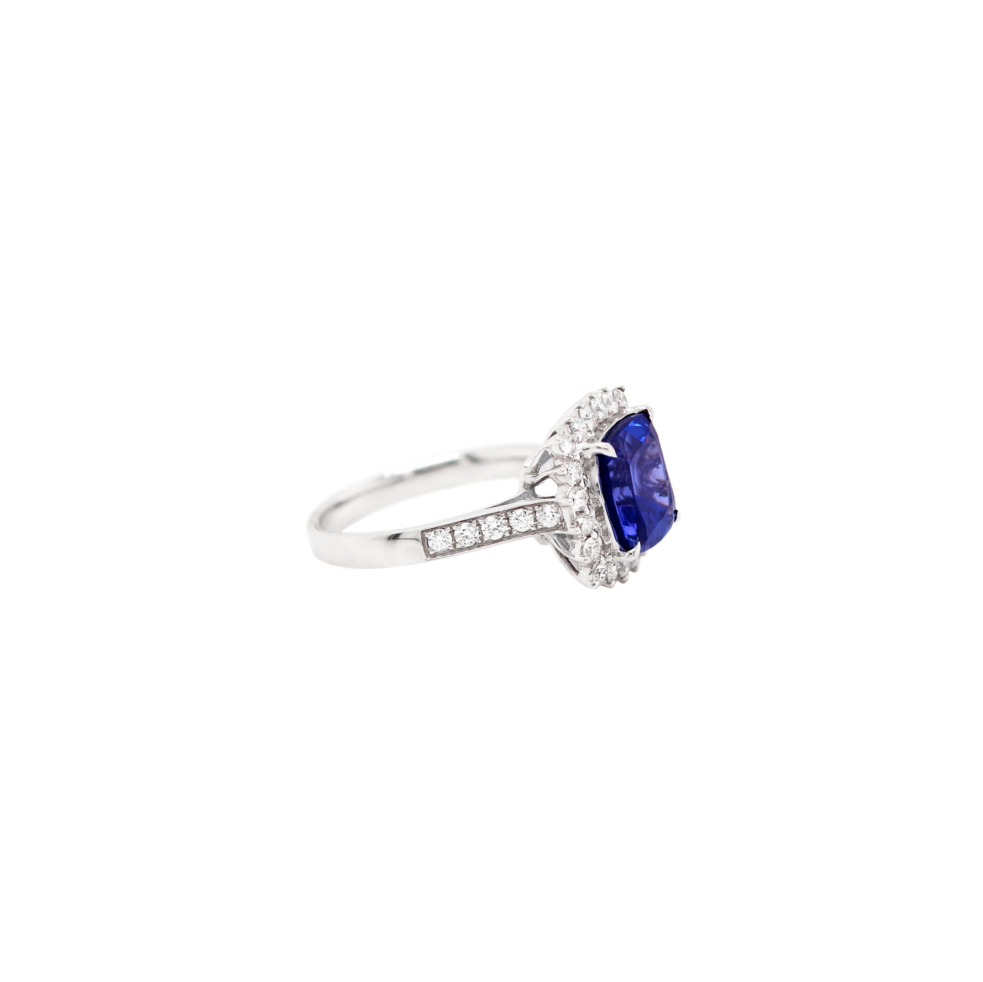 This lovely ring features a vivid blue cushion shaped tanzanite weighing 4.20ct in a four claw, open back setting. The beautiful stone is surrounded by 20 round brilliant cut diamonds in open back three claw settings and further set with 5 round