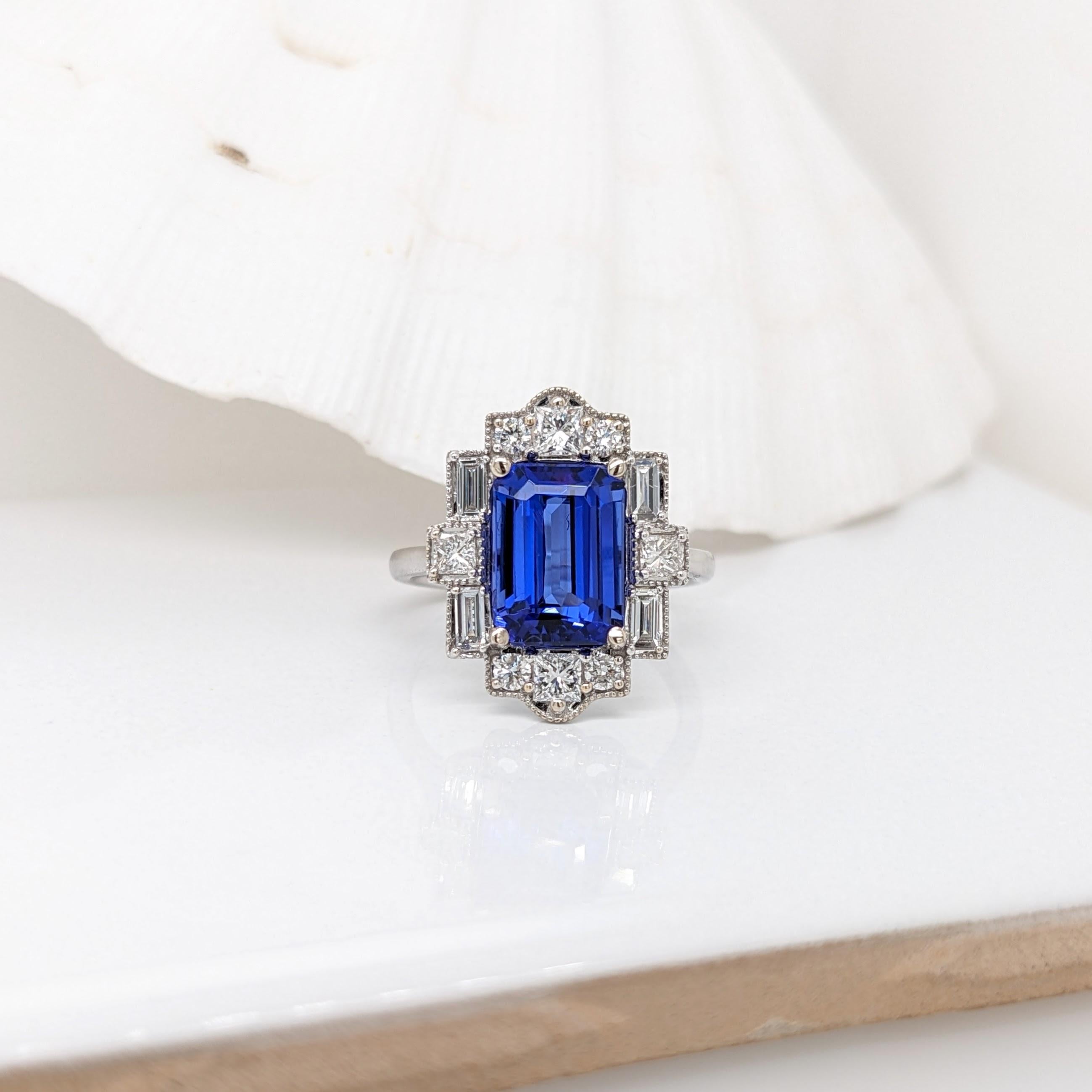 A gorgeous art deco style ring featuring an emerald cut tanzanite with a rich blue color that can compete with a stunning sapphire! An original ring design featuring a halo of mixed diamond shapes and milgrain detailing all in 14k white gold, this