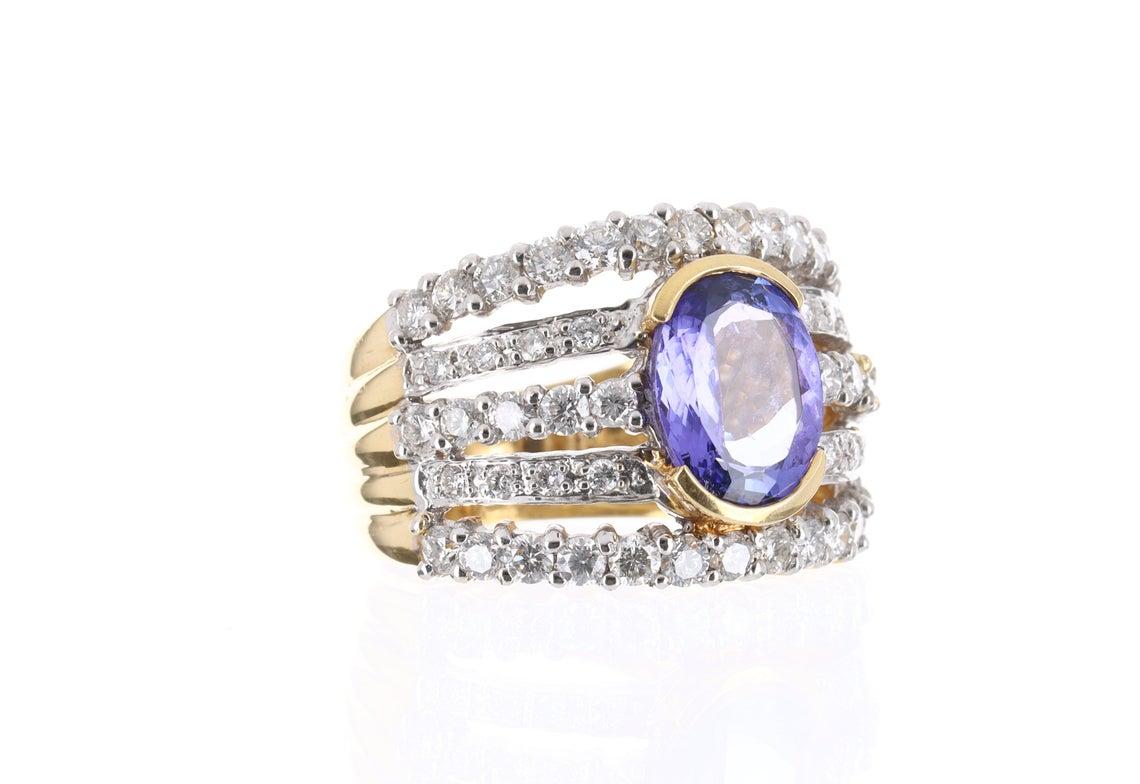 Elegantly displayed is a tanzanite and five-row diamond cocktail ring in solid 18K gold. This ring features a brilliant, violet tanzanite with exceptional eye clarity and luster. The oval is set in a fashionable cluster styled setting. The diamonds