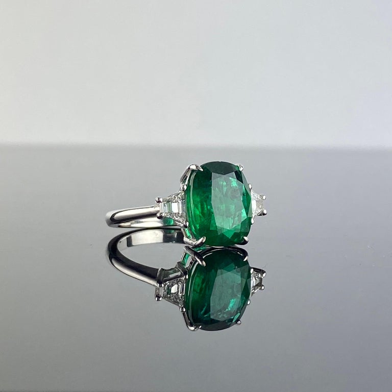 A stunning 4.25 carat cushion shaped, Zambian Emerald, transparent with an ideal vivid green color, set with 0.35 carat trapeze White Diamonds. The ring is made using solid 18K White Gold, sized at US 7, but can be altered. 
Please message for more