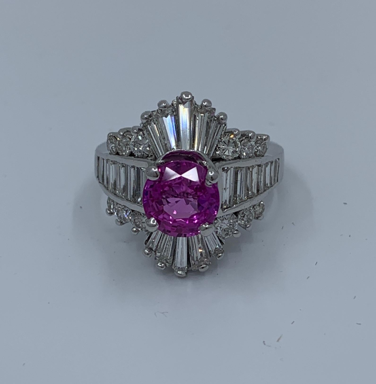 A vivid purplish pink round brilliant cut natural corundum sapphire is GIA Certified and is prong set in 14 karat white gold.   It is surrounded by prong and channel set long tapered and straight baguette diamonds and accented by prong and tension