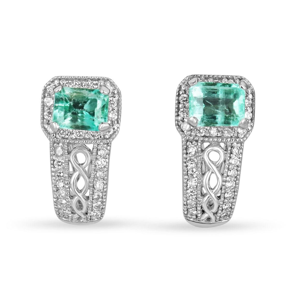 A divine pair of emerald and diamond omega styled earrings. Fashioned in pure, 14K white gold, the center of attention are glorious emerald cut shaped emeralds. Each stone is handset in a simple four-prong setting. The emeralds portray excellent
