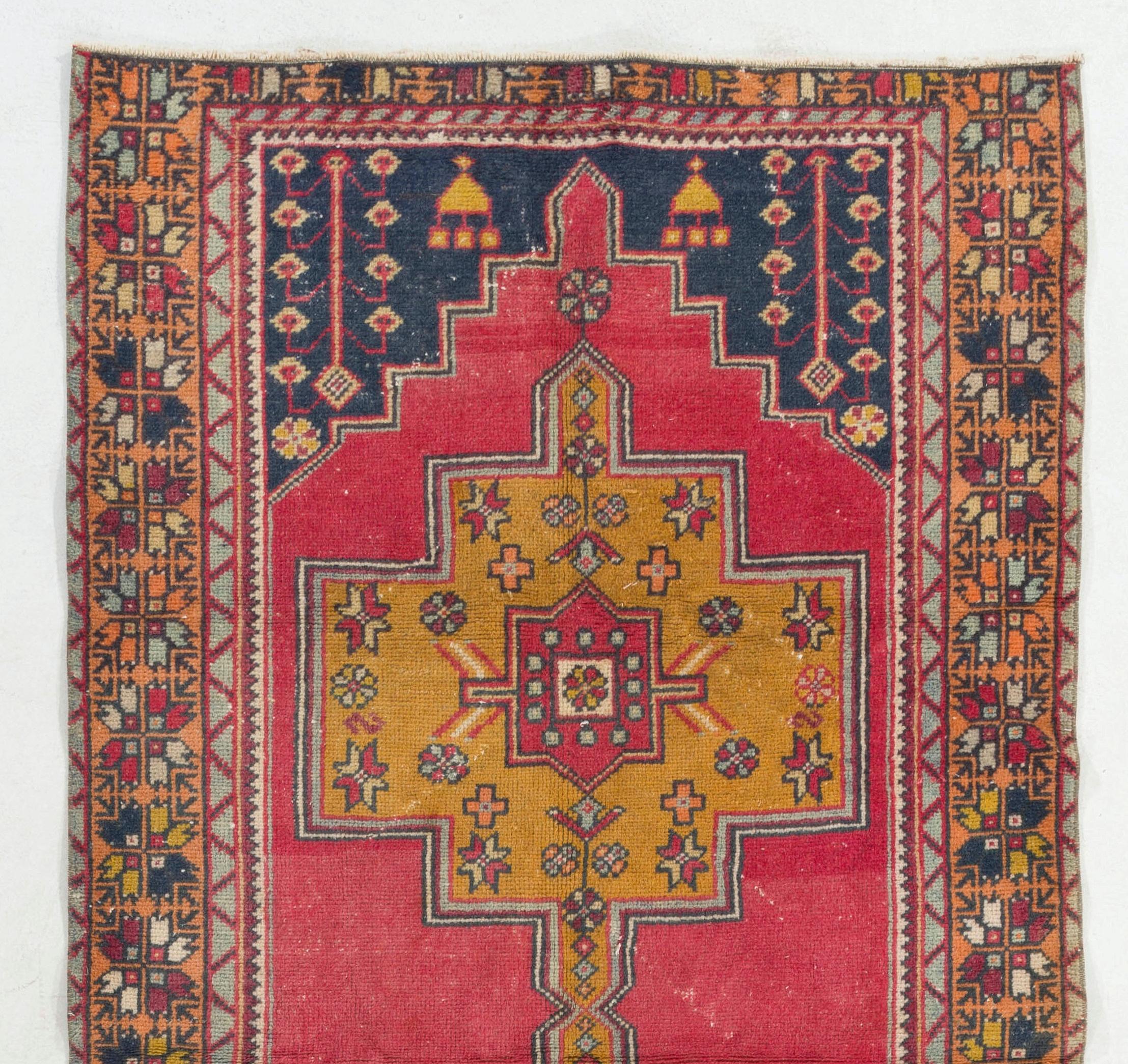 This vintage Central Anatolian area rug has two linked geometric medallions at its centre in deep, saturated gold that are decorated with abstract stars and floral heads against a plain field in bright red. The corner-pieces in dark indigo are