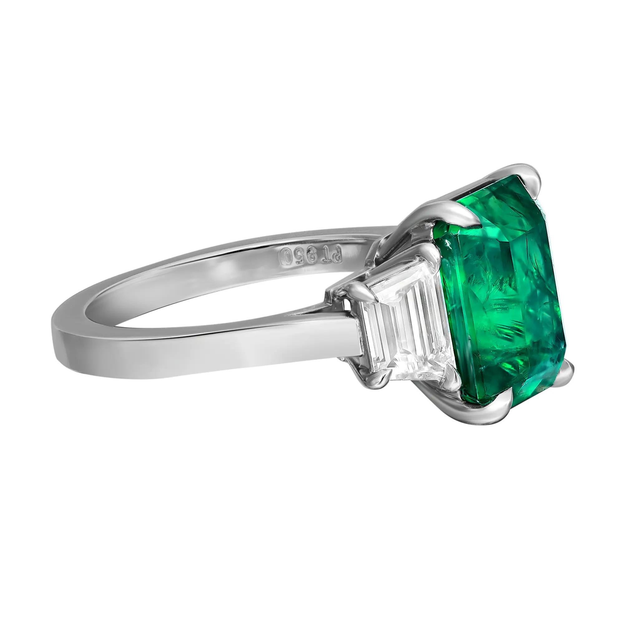 This luxurious three-stone engagement ring features a stunning 4.30 carats GIA certified octagonal Zambian green Emerald as the center stone with 0.83 carat of trapezoid-cut diamonds on each side in prong setting. The octagonal cut gives the emerald