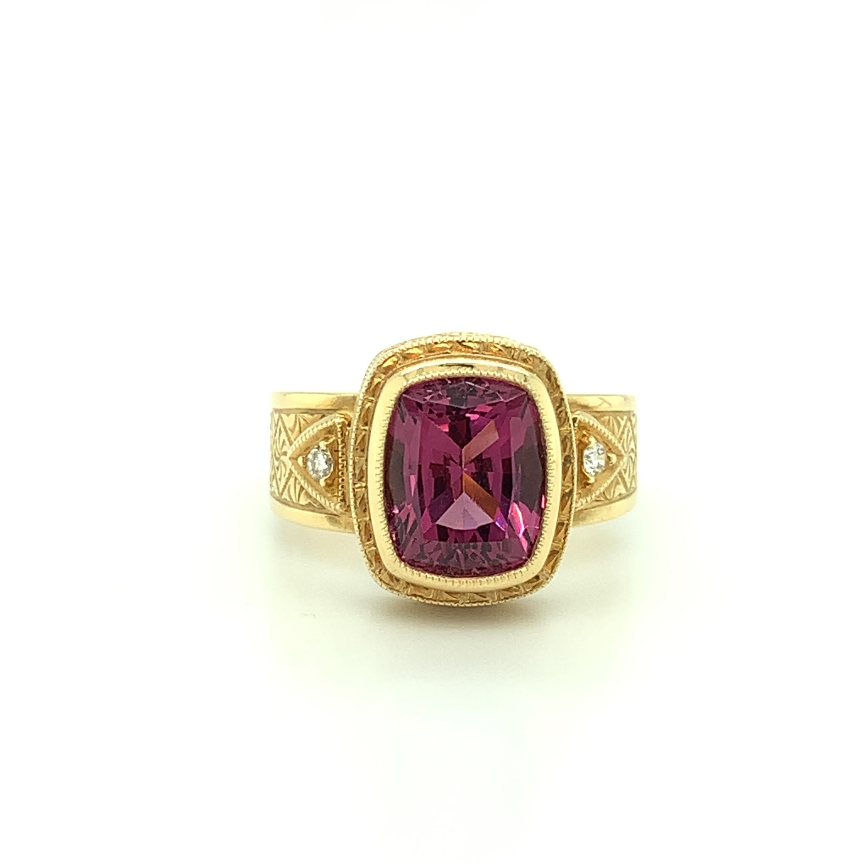 A gorgeous 4.30 carat raspberry-red rhodolite garnet is featured in this handsome ring. The cushion-cut center gem sits in an 18k yellow gold bezel that has been intricately hand engraved, displaying a level of artisanship and skill rarely seen