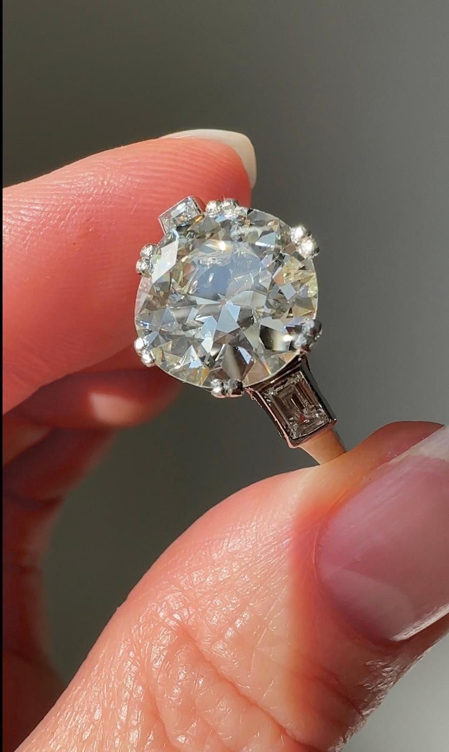 This exceptionally lovely vintage ring centers on a scintillating 4.37 carat European-cut diamond (accompanied by an HRD Antwerp certificate stating SI2 clarity with K color) that beams from between a pair of mirror-like baguette diamonds. The